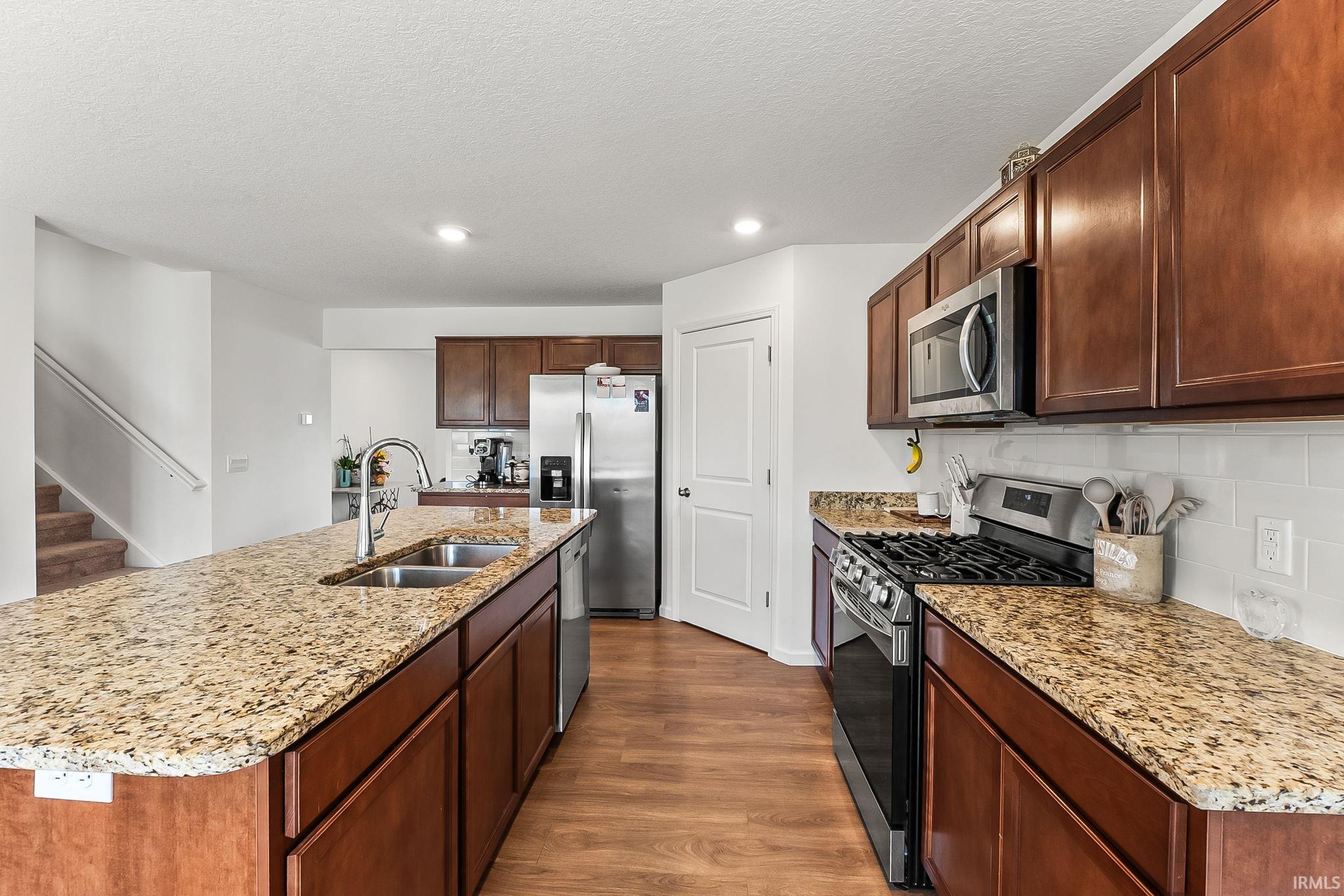 Kitchen featuring a large island with an undermount double-basin sink, granite countertops, wood-finish flooring, stainless steel appliances, and wood cabinetry