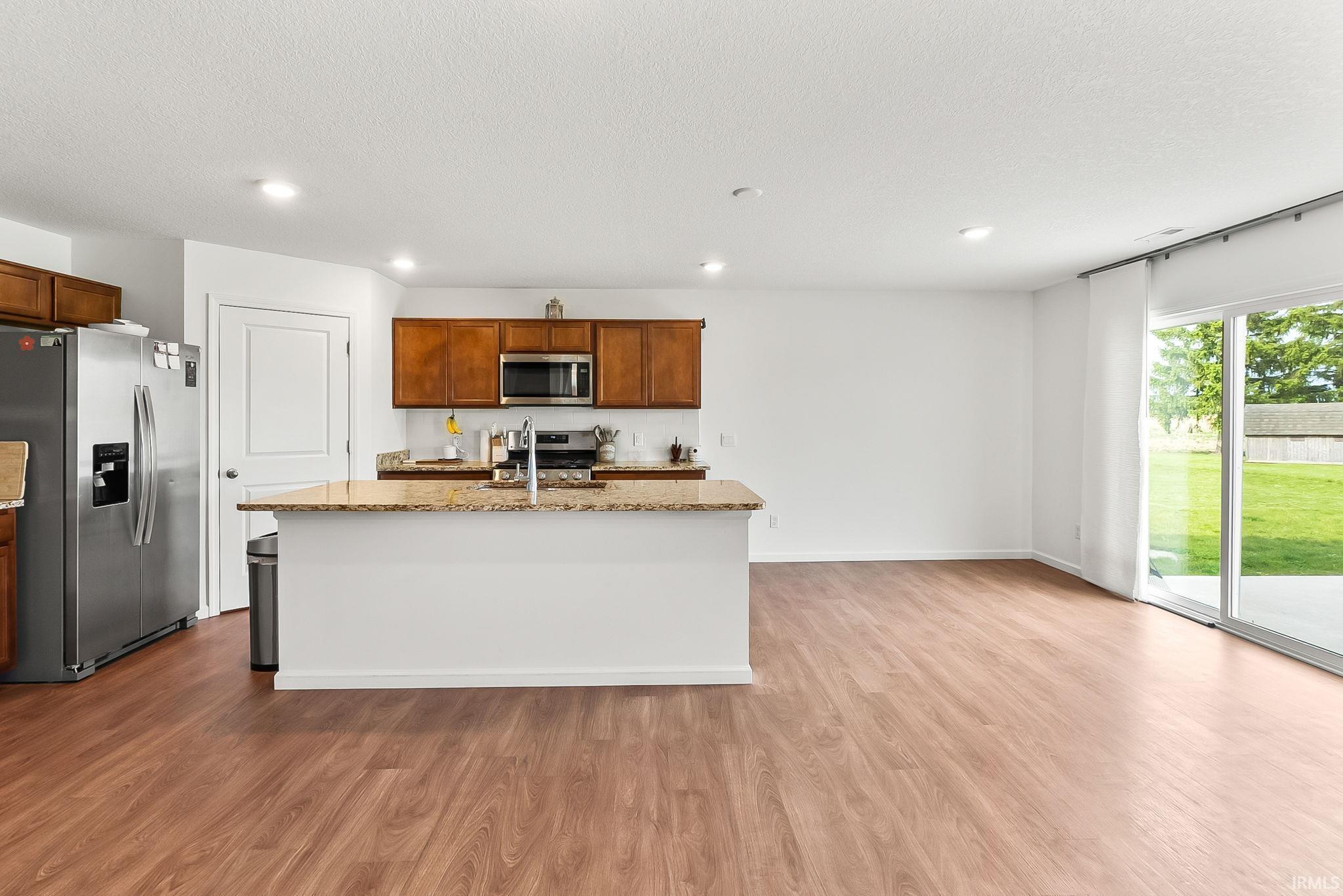 Open-concept kitchen and living area featuring wood-finish flooring, recessed lighting, and a sliding glass door to the exterior