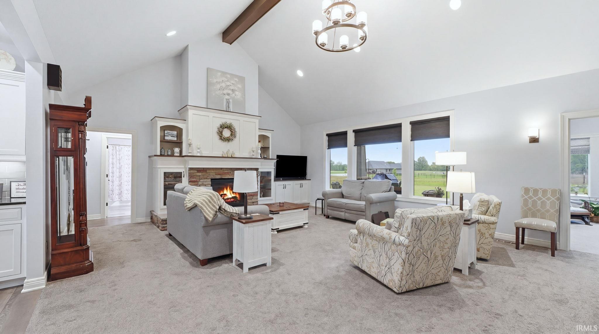 Spacious living area featuring a vaulted ceiling with exposed wood beams, a stone fireplace with built-in cabinetry, large windows, and a chandelier light fixture