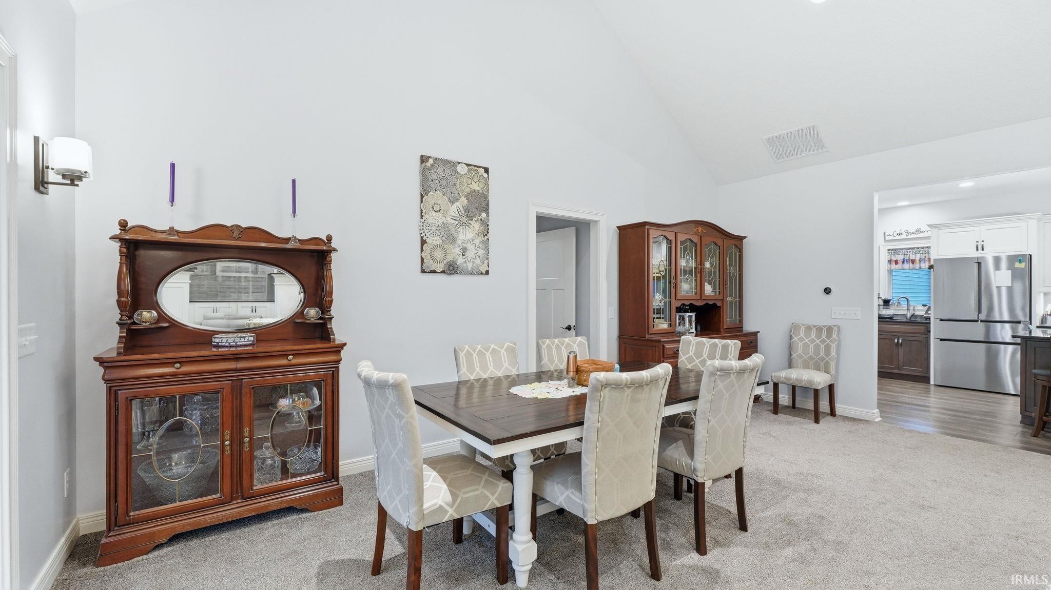 Vaulted ceilings enhance this dining area, featuring plush carpeting and a wall-mounted sconce