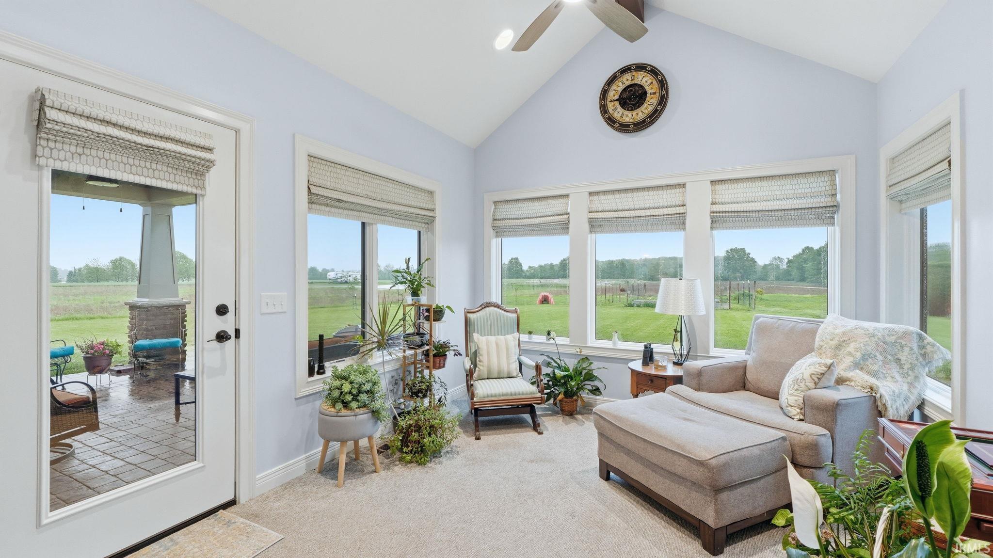 Sunroom featuring vaulted ceilings, a ceiling fan, broad windows, and a glass-paneled door leading to a covered patio with stone-wrapped columns