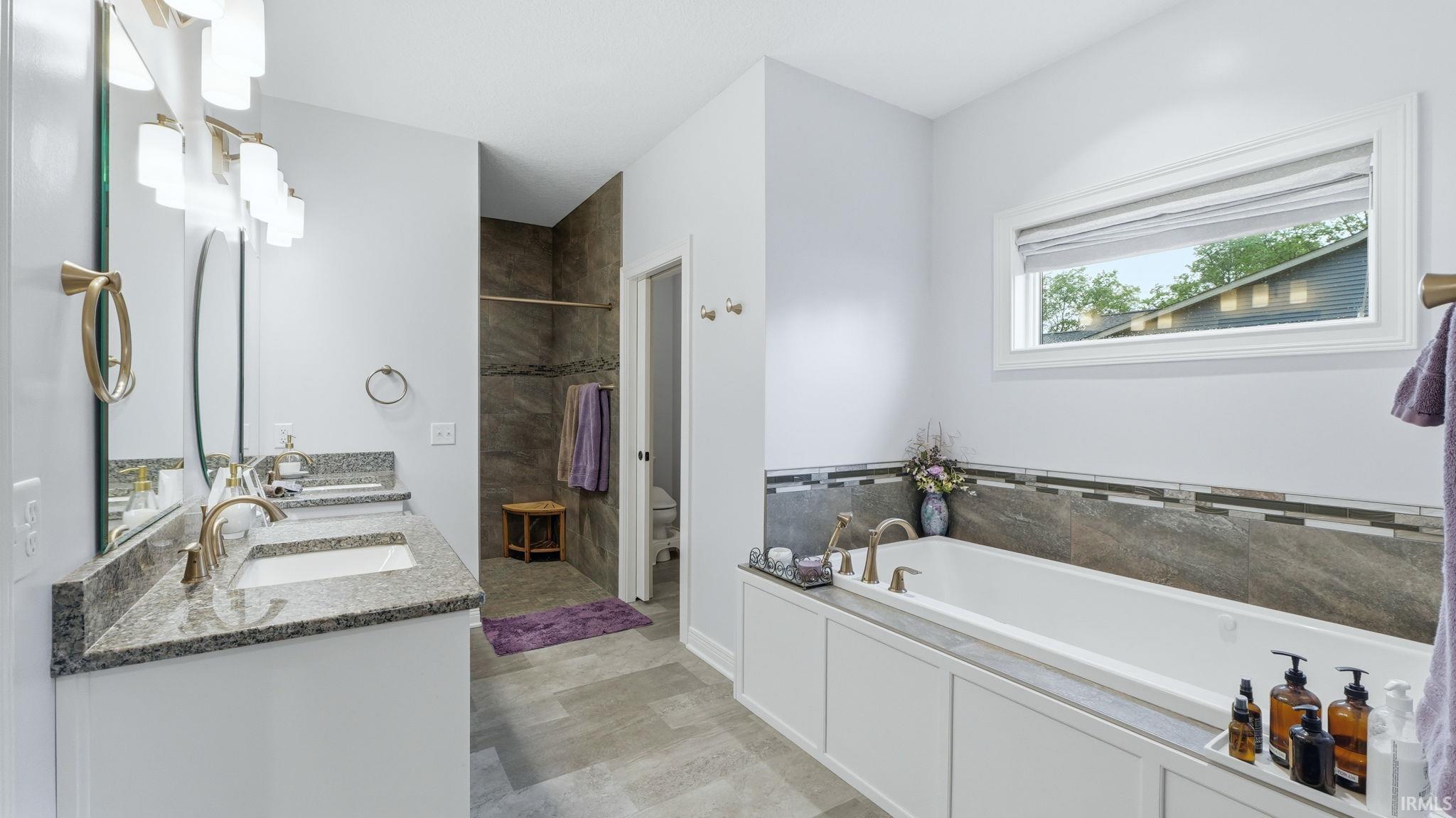 Spacious bathroom featuring a dual vanity with granite countertops, an undermount sink, and gold-toned fixtures