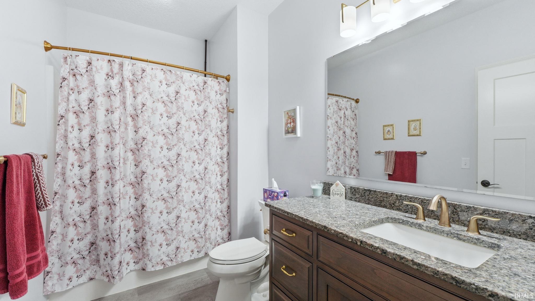Bathroom featuring a dark wood vanity with a granite countertop, undermount sink, and brass-finish fixtures
