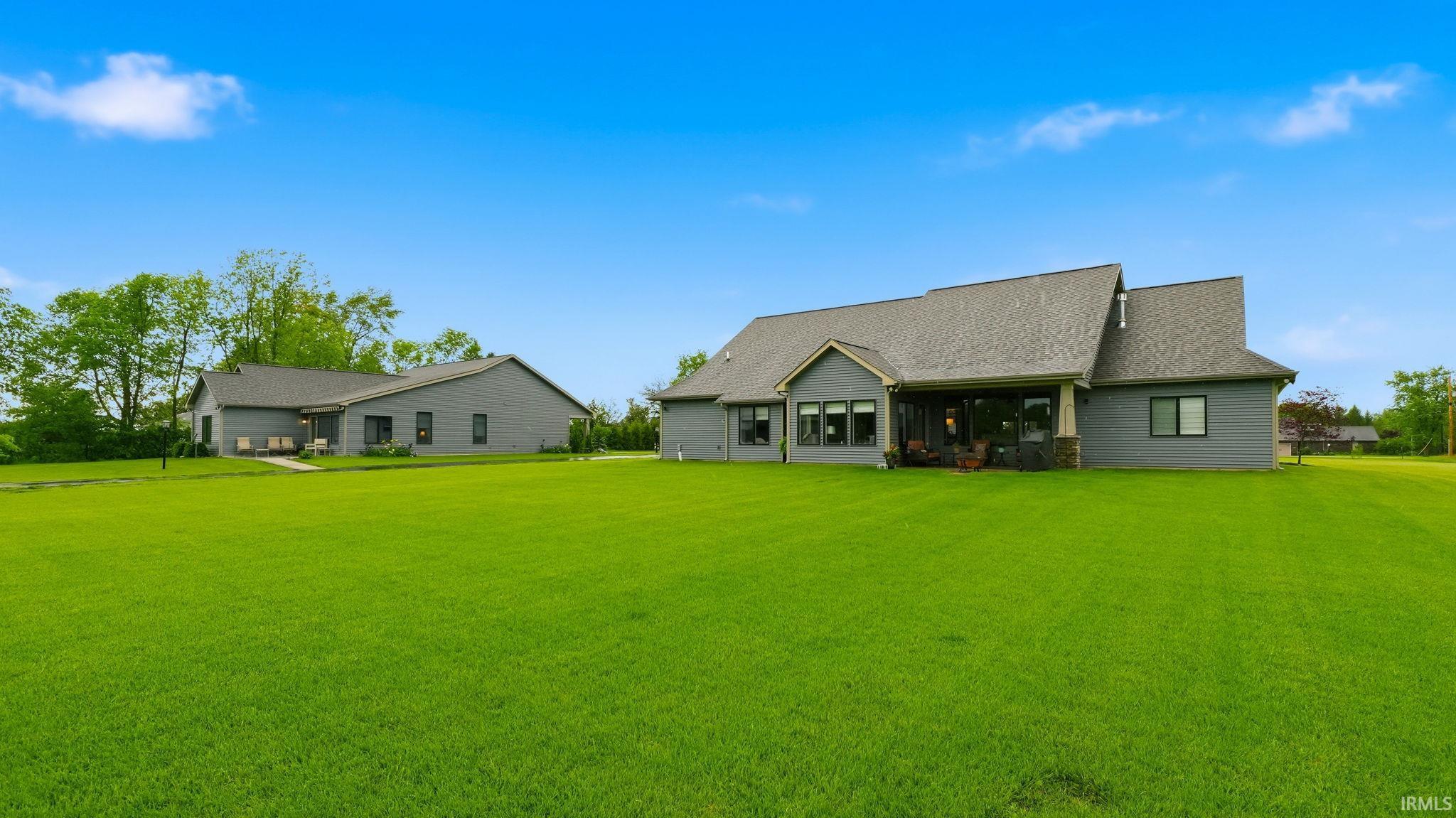 Expansive green lawn surrounds a gray-sided residence with multiple windows and a covered patio area