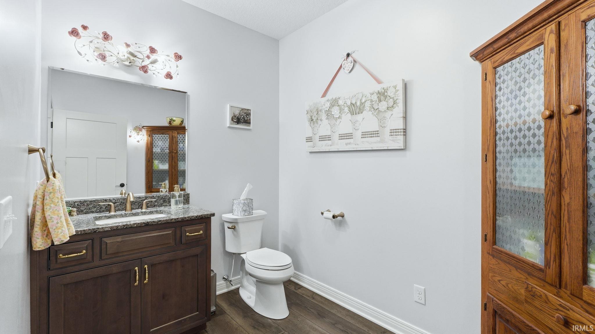 Powder room featuring a dark wood-finish vanity with a granite countertop and undermount sink, brass-finish faucet, and an ornate light fixture