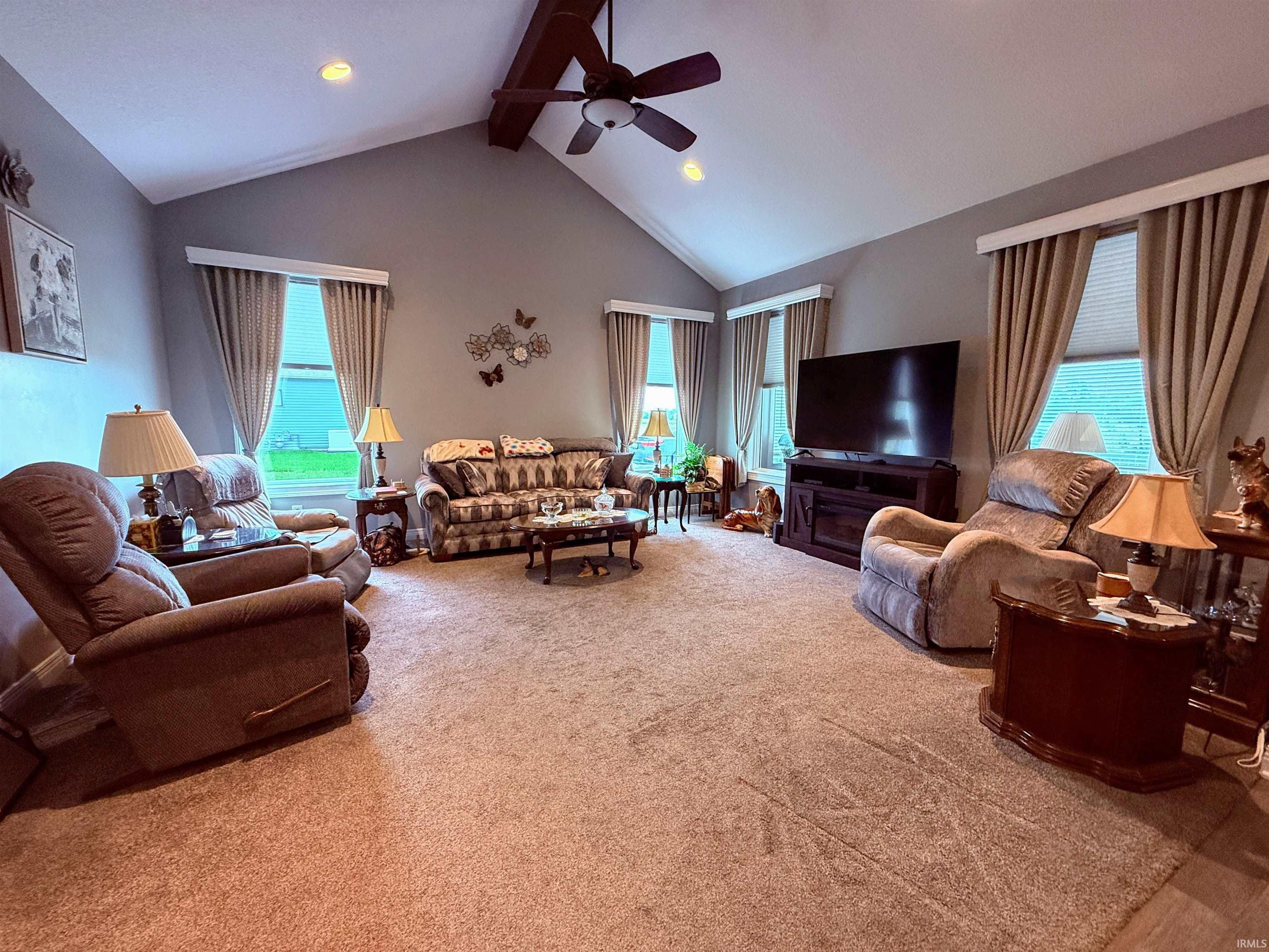 Spacious living area featuring a vaulted ceiling with exposed wood beam, recessed lighting, and a ceiling fan
