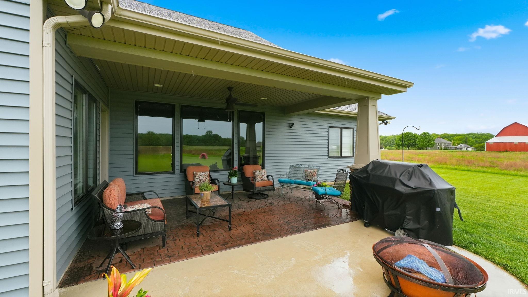 Expansive covered patio featuring a stamped concrete surface, light blue siding, exterior lighting, and large windows
