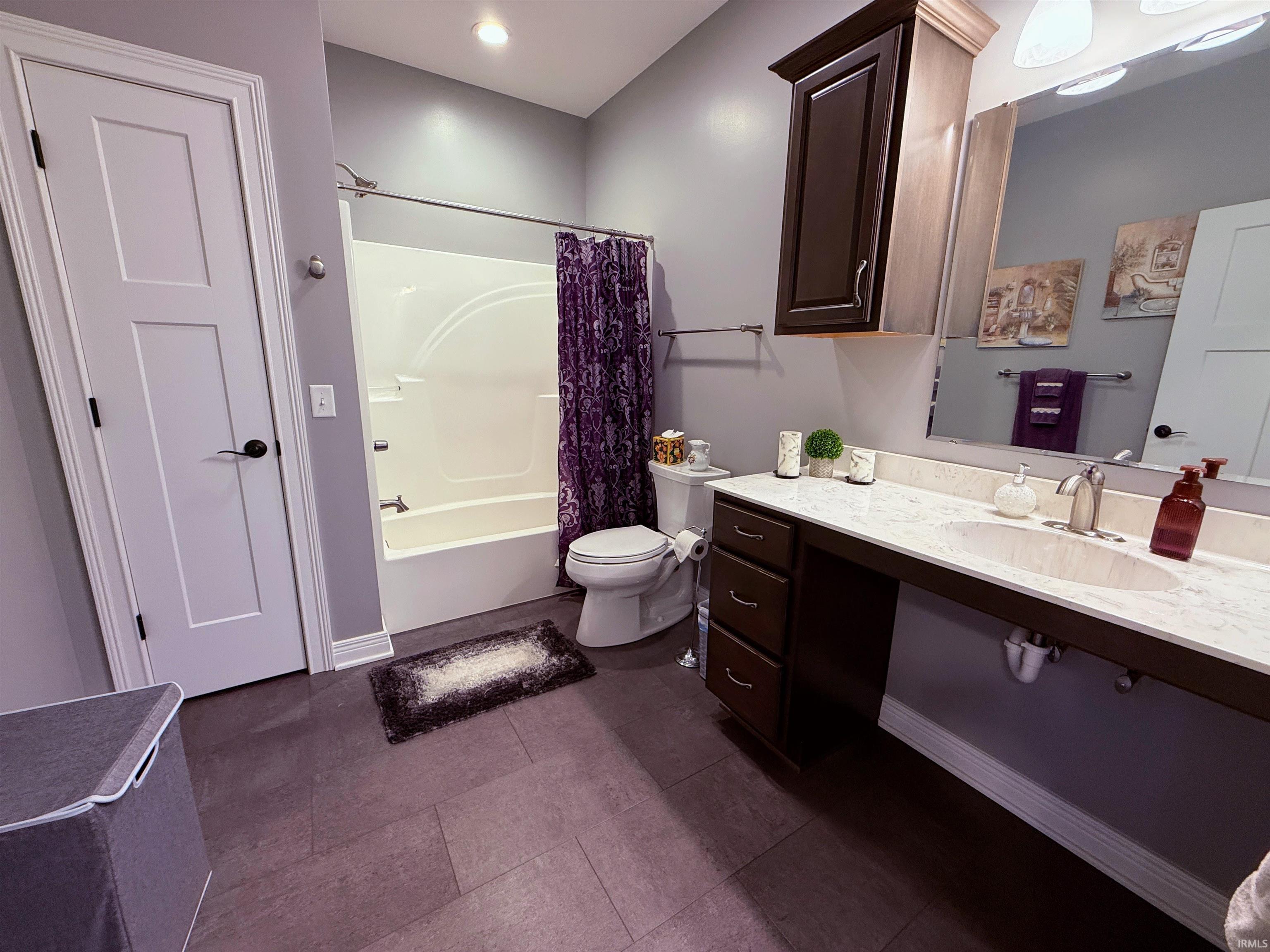 Bathroom featuring a white bathtub and shower combination, dark tile flooring, a single vanity with a light-colored countertop, and a wall-mounted mirror