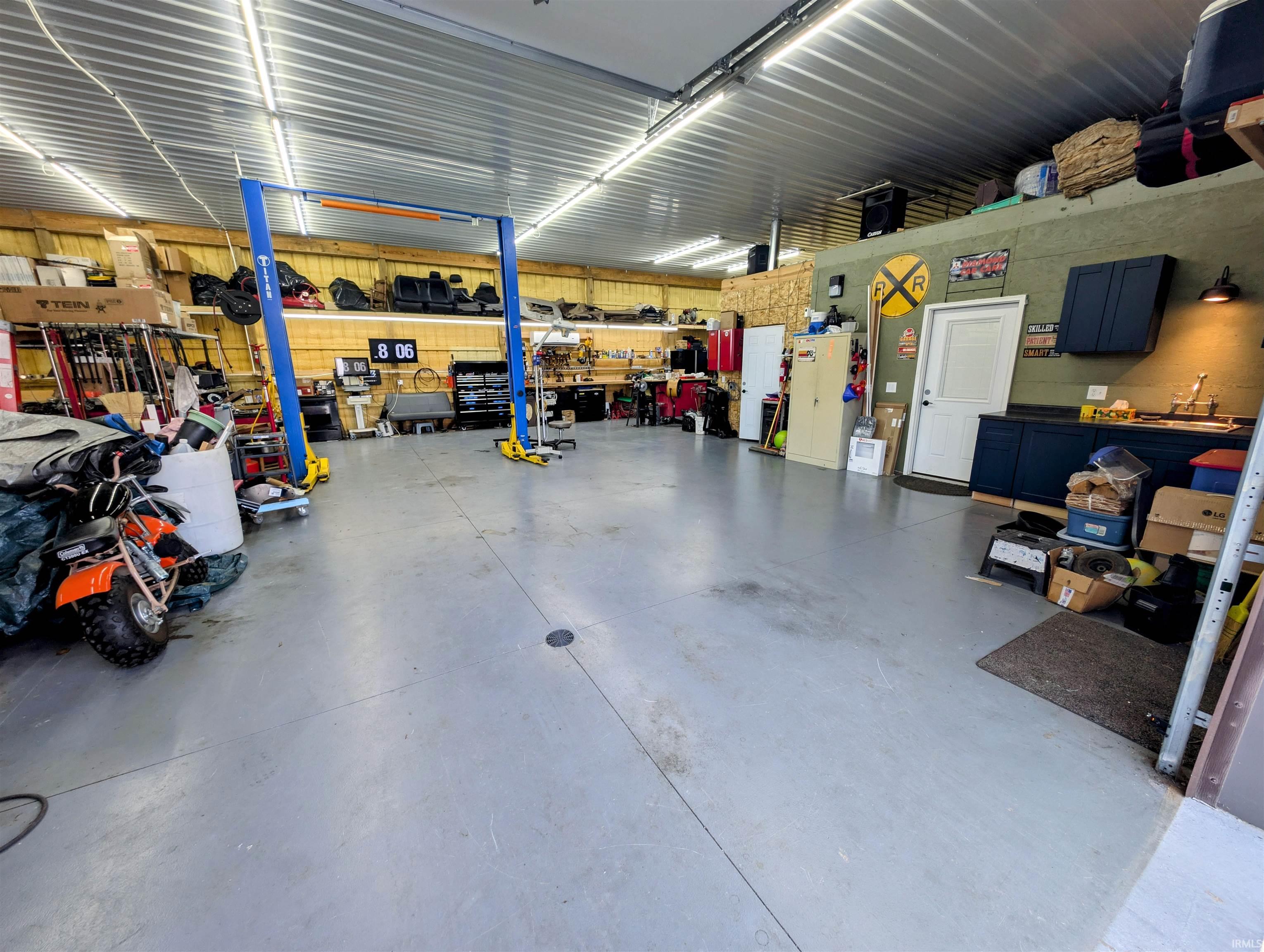 Spacious garage with high ceilings, concrete flooring, ample overhead lighting, built-in cabinetry with a sink, and vehicle lift