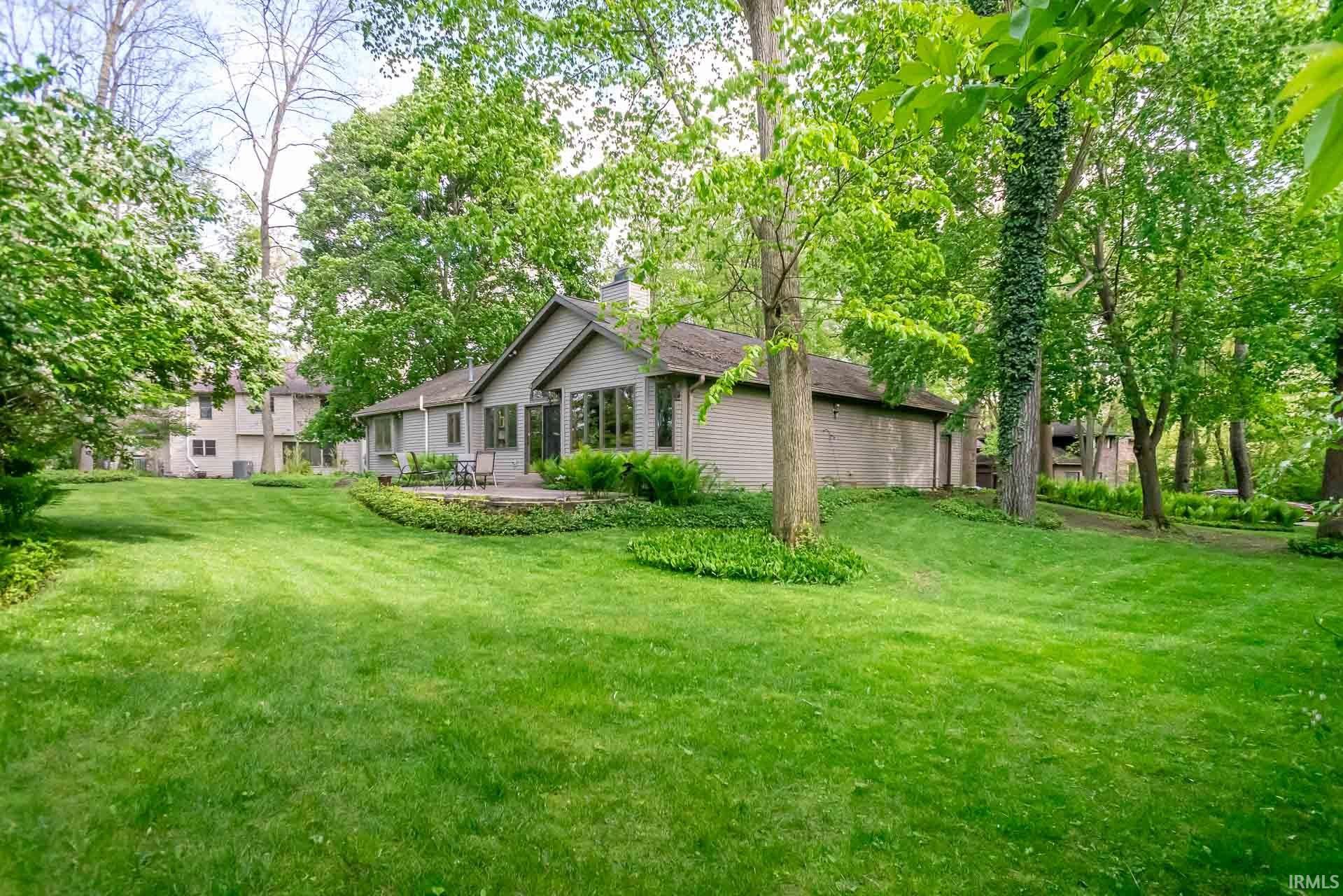 Expansive rear lawn featuring mature trees and a stone patio