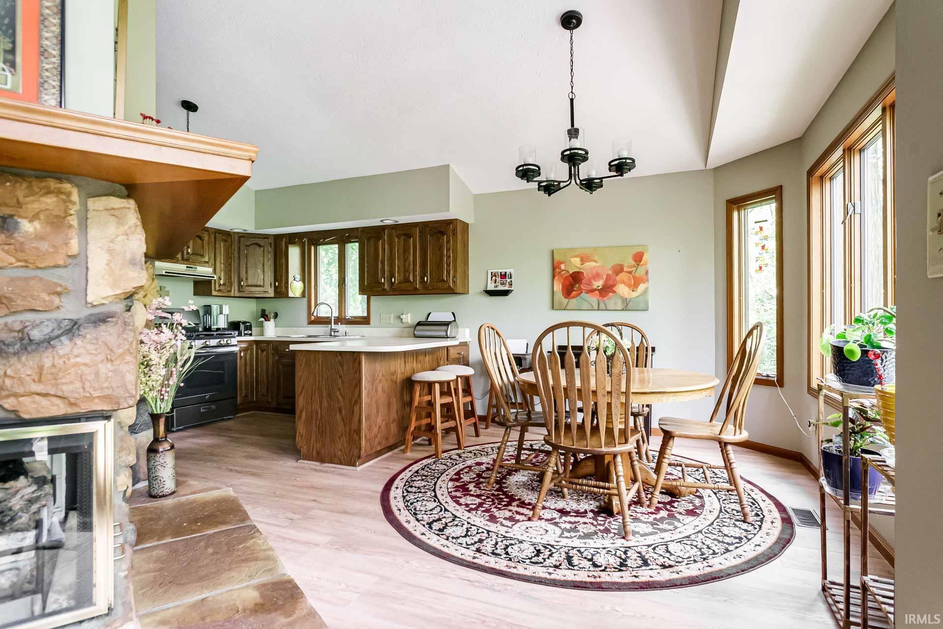 Open-concept kitchen and dining area featuring wood-finish flooring, a stone-faced fireplace with a mantel, and a kitchen island with seating