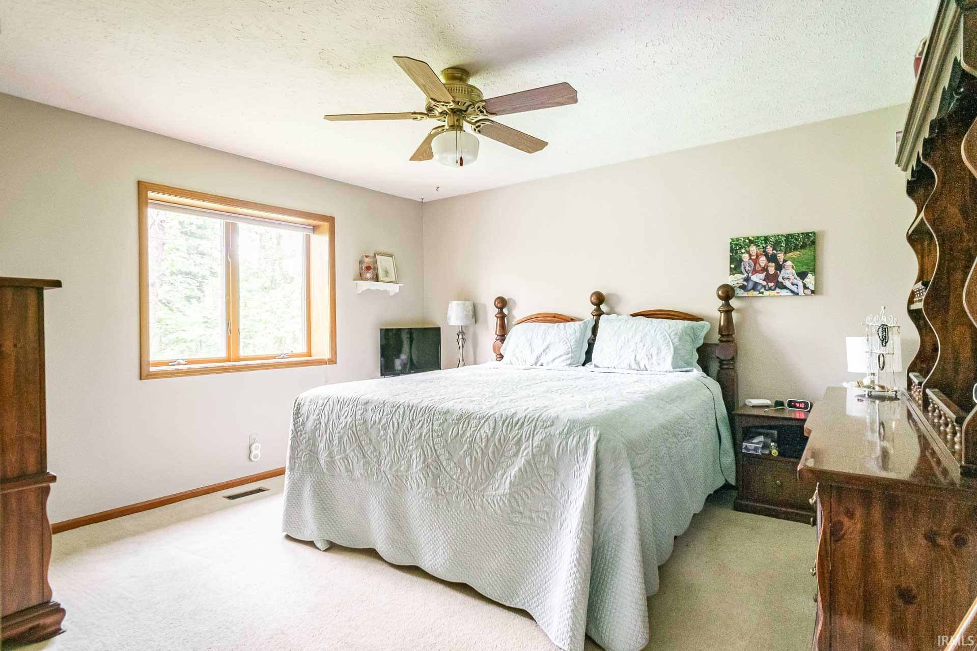 Carpeted room featuring a ceiling fan with light fixture, a large window with wood trim, and a wall-mounted shelf