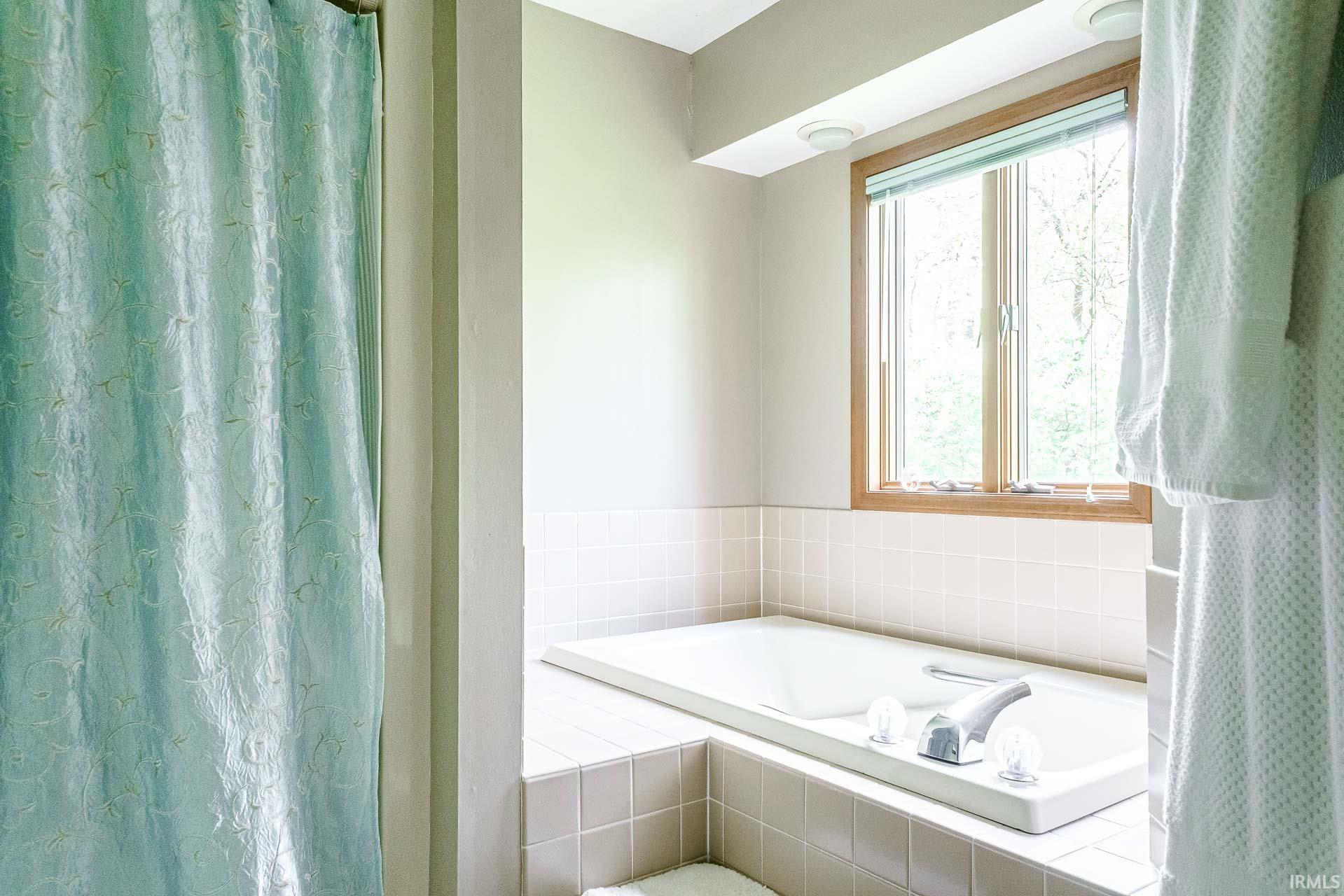 Built-in soaking tub with chrome fixtures, surrounded by light-toned square tile