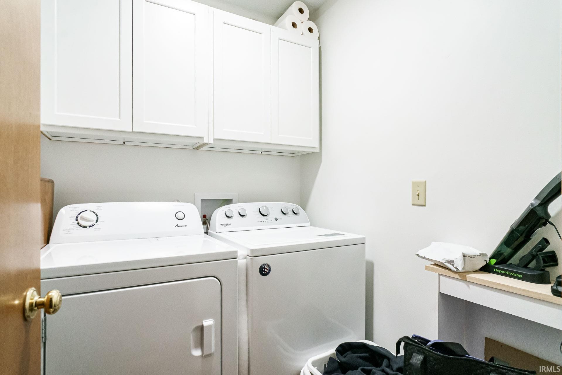 Dedicated laundry area featuring white upper cabinetry, a light wood-finish door, and a built-in white countertop