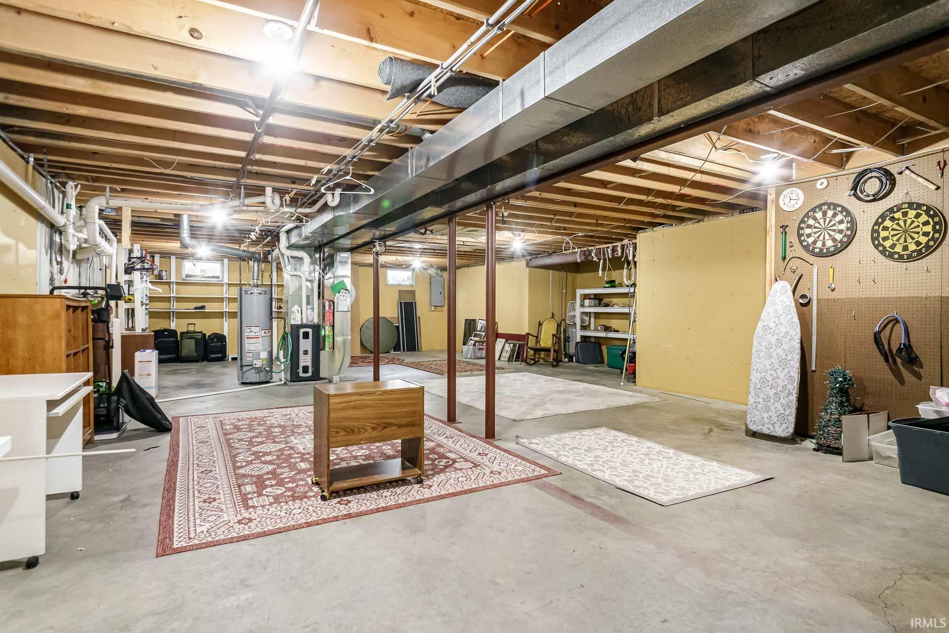 Expansive unfinished basement featuring concrete flooring, exposed ceiling joists, overhead ductwork, multiple utility connections, and built-in shelving