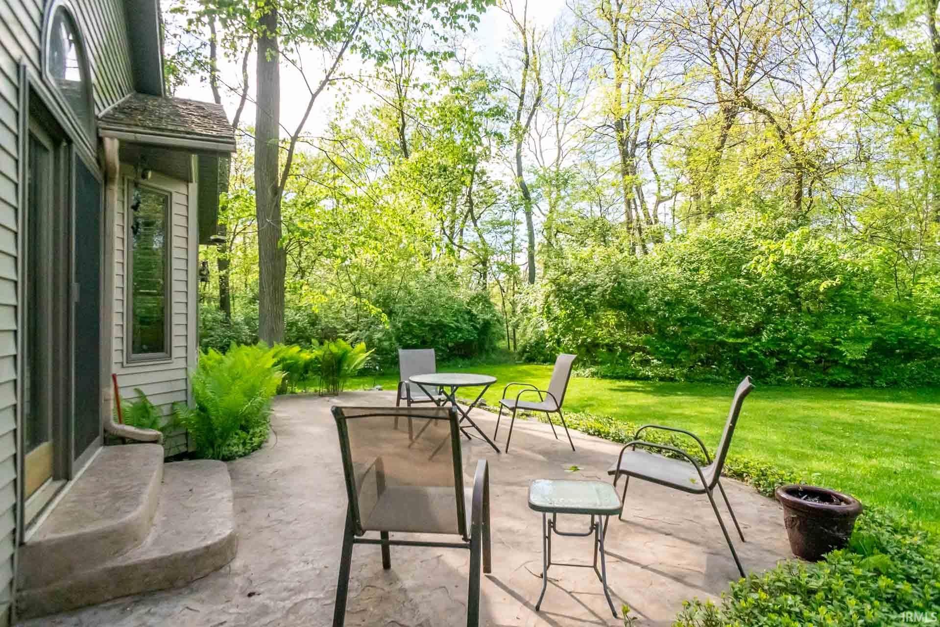 Private patio area featuring a concrete surface, lush green lawn, mature trees, and established perimeter shrubbery