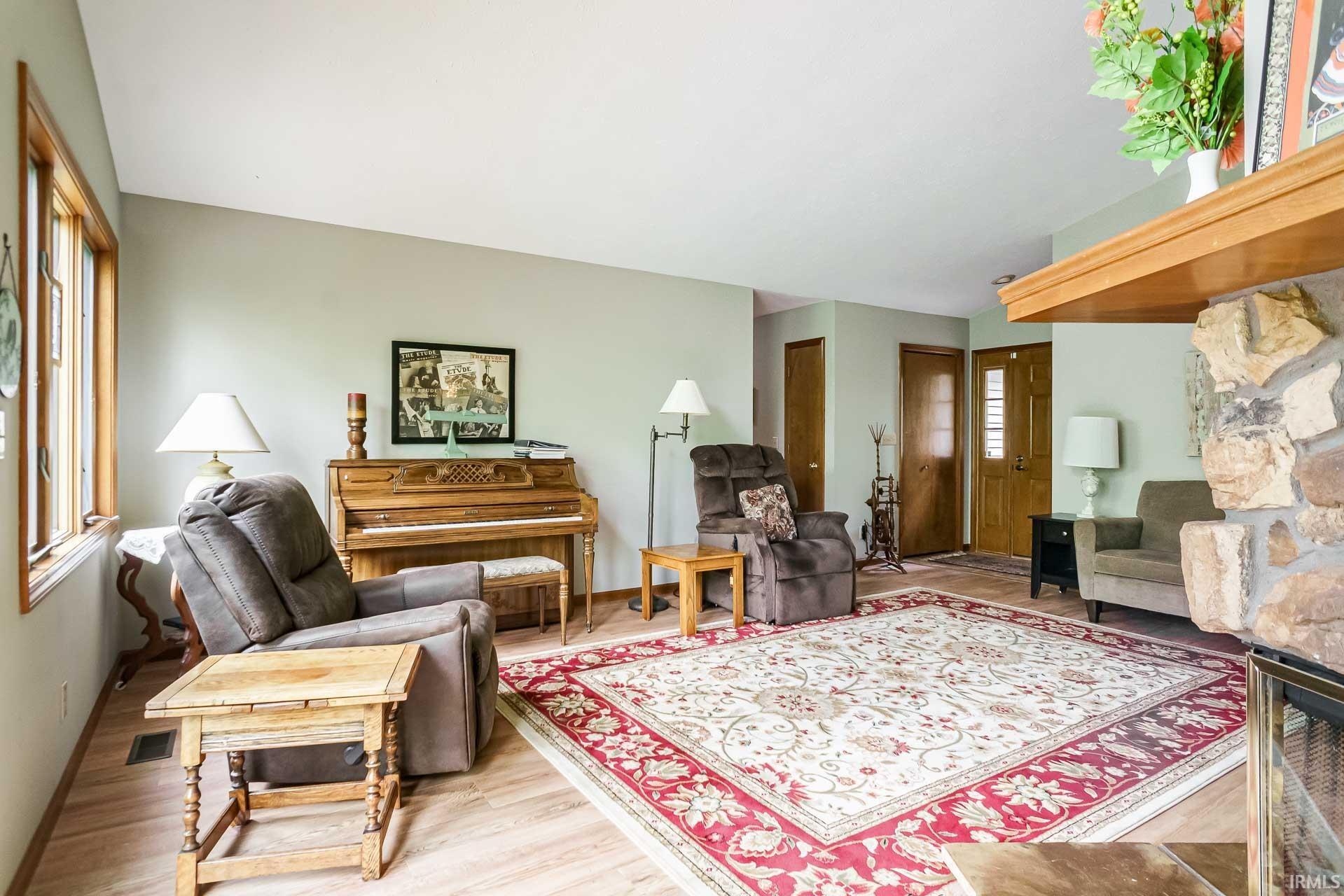 Spacious living area featuring light wood-finish flooring, a stone-clad fireplace with a wood mantle, and multiple windows