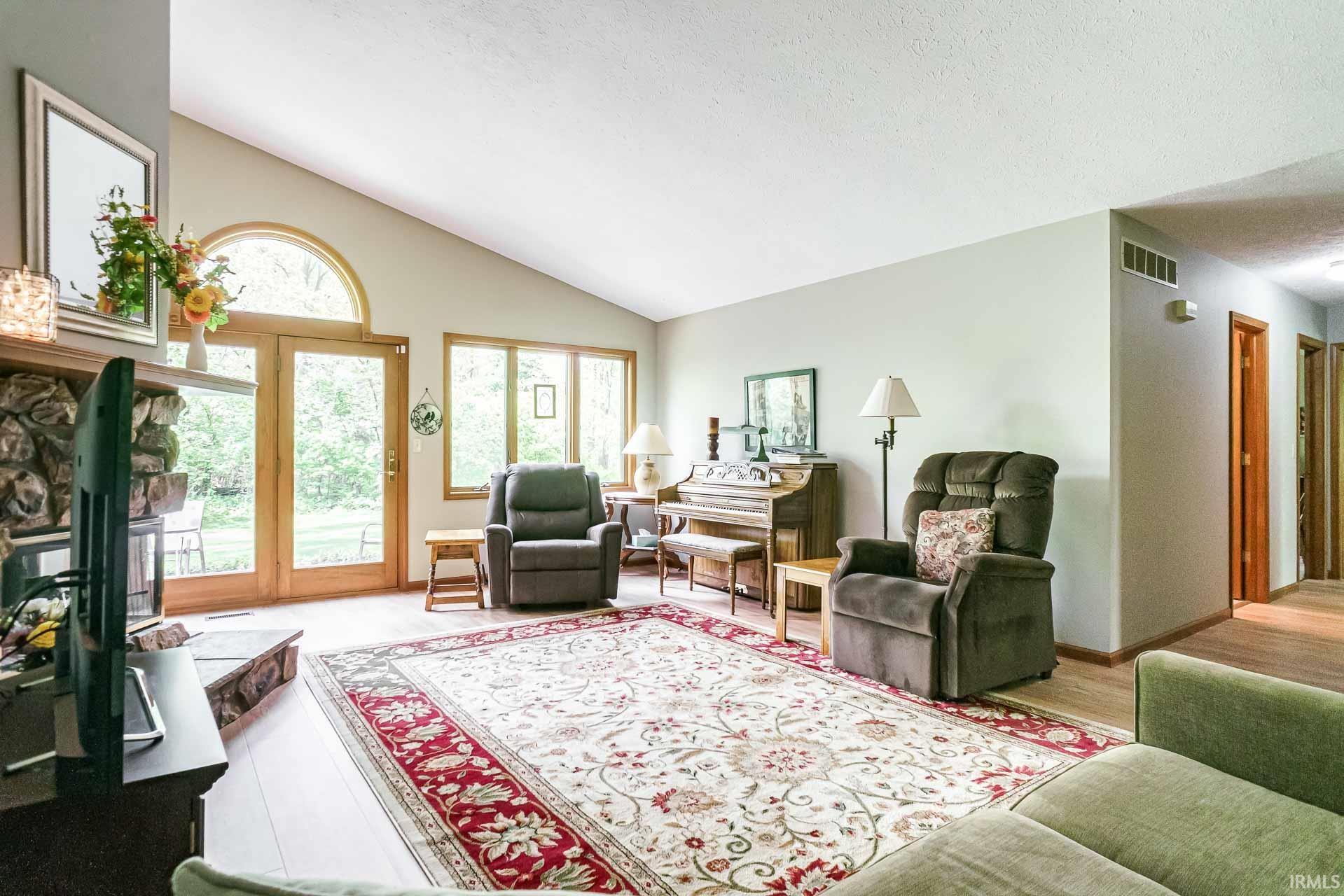 Living space featuring a vaulted ceiling, stone fireplace, wood-finish flooring, and French doors with an arched transom