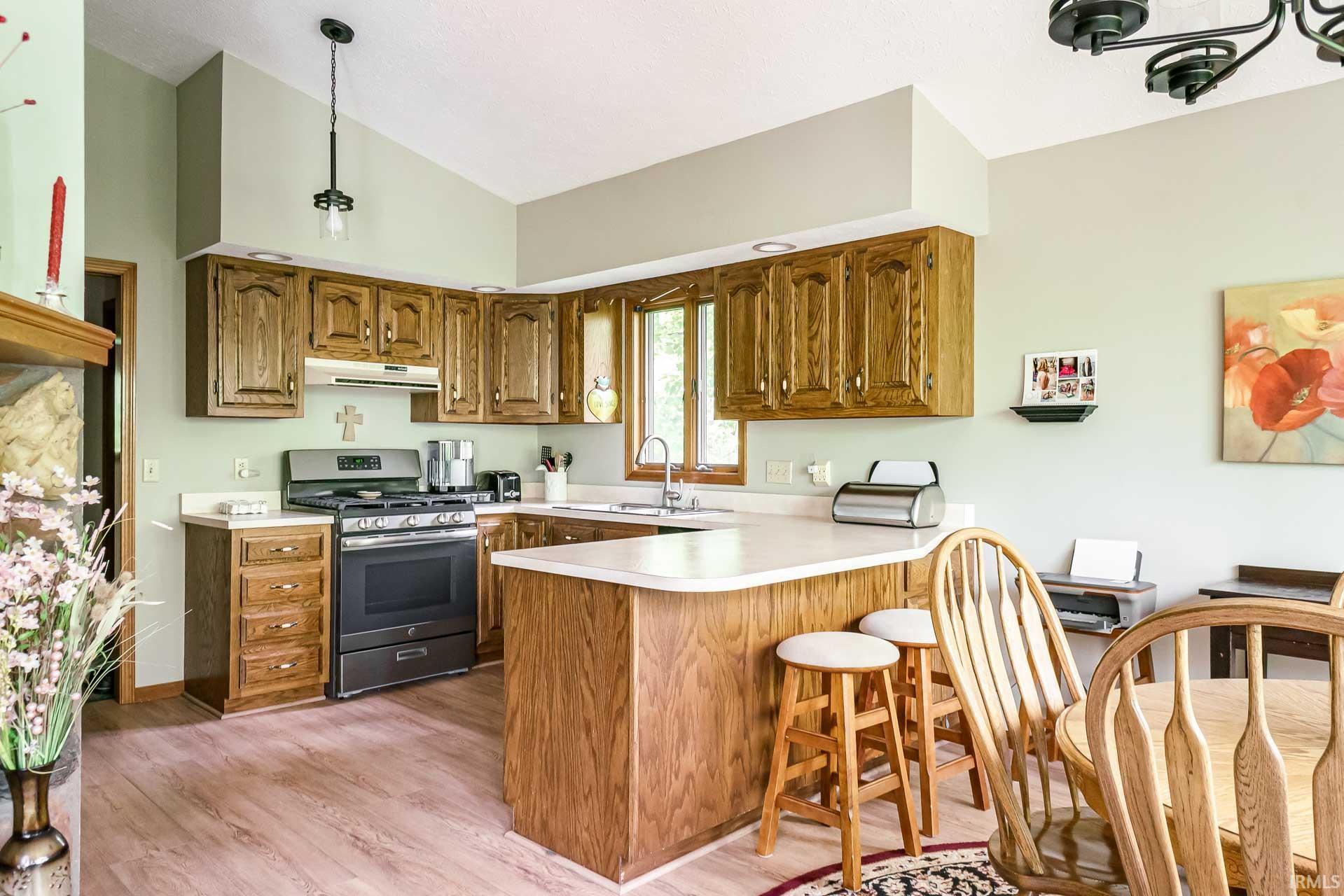 Kitchen featuring wood-finish cabinetry, stainless steel range, and a corner sink with window