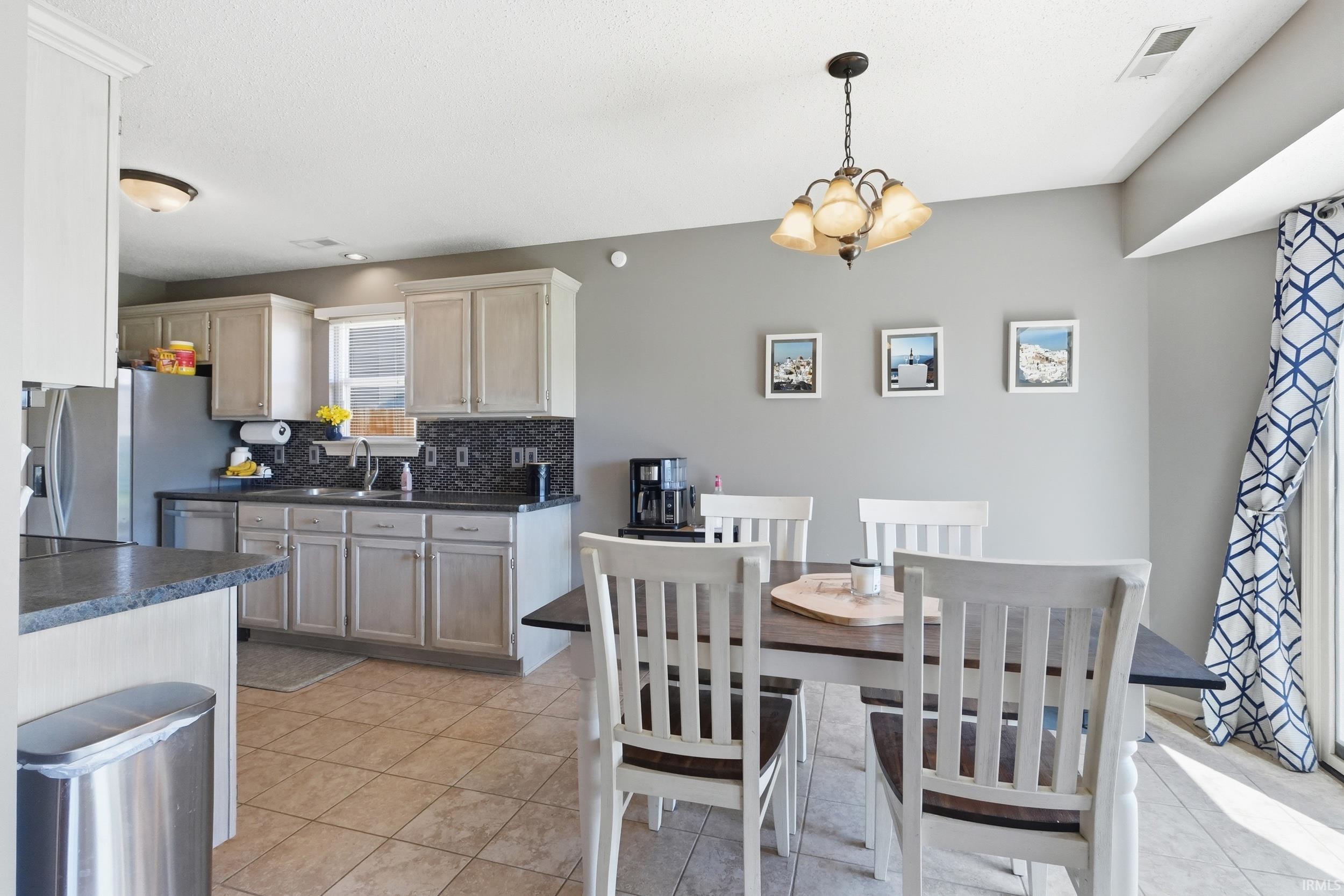 Open-concept kitchen and dining area featuring light-toned cabinetry, dark countertops, and a dark mosaic tile backsplash