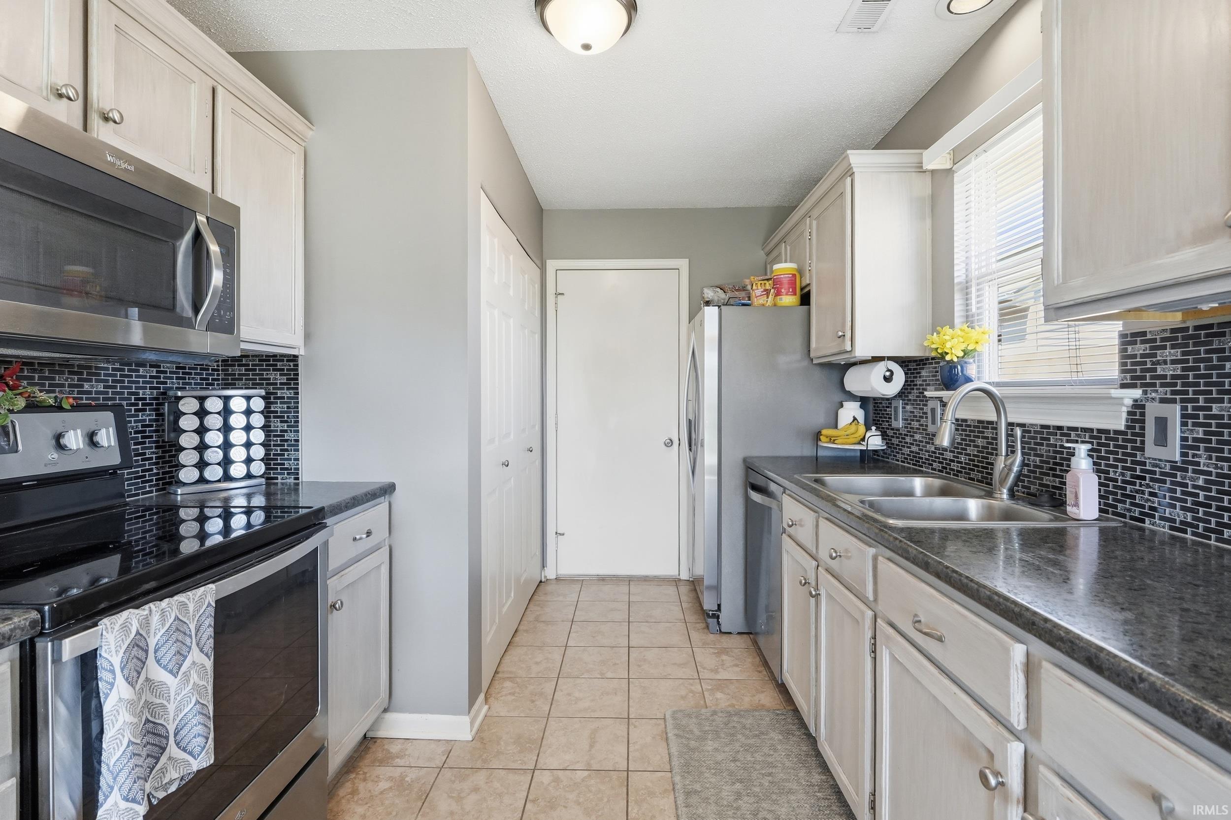 Galley kitchen featuring light-toned cabinetry, dark countertops, and a full suite of stainless steel appliances