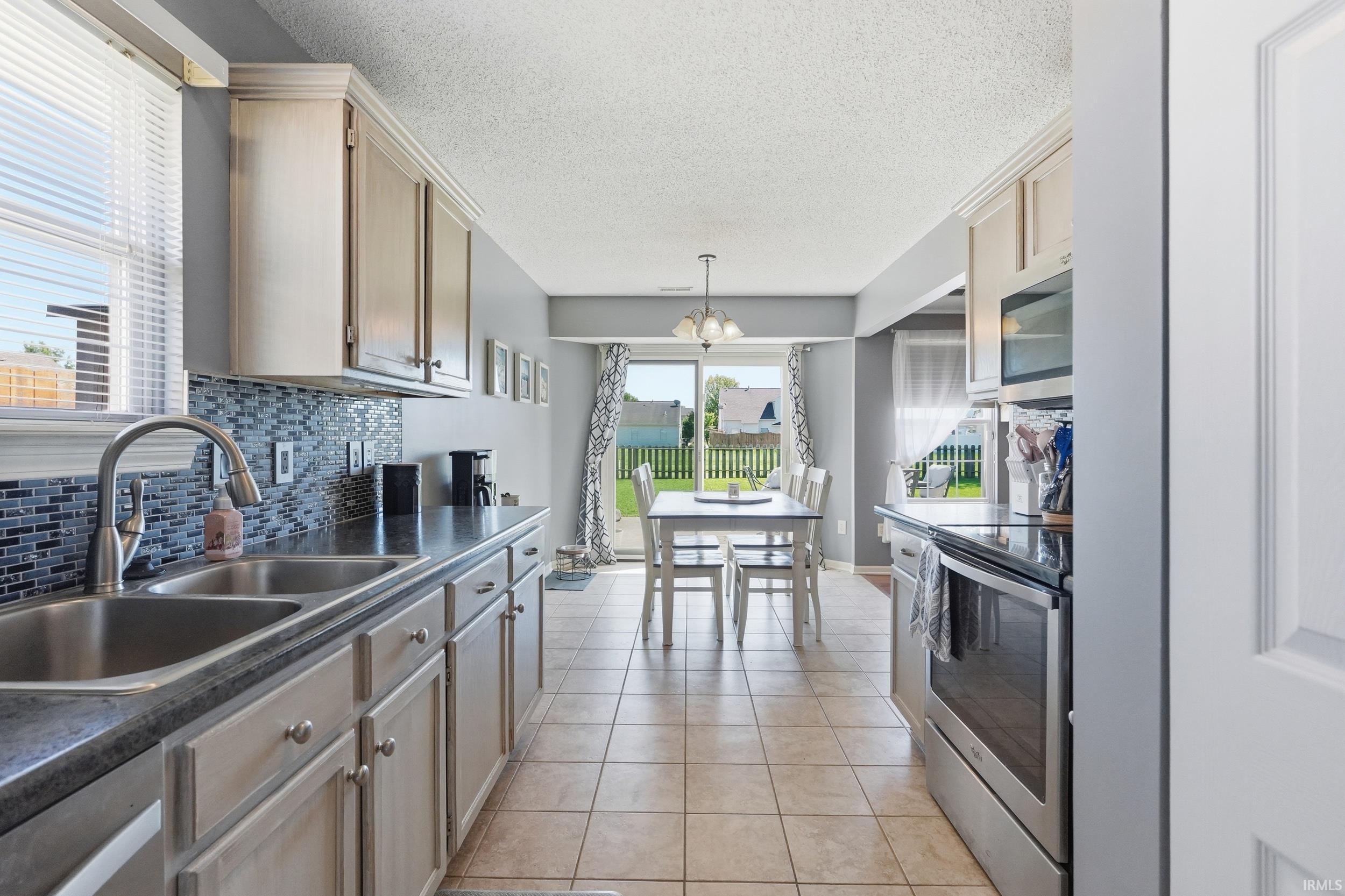Kitchen featuring light wood-finish cabinetry, a dual basin stainless steel sink with a high-arc faucet, and a mosaic tile backsplash