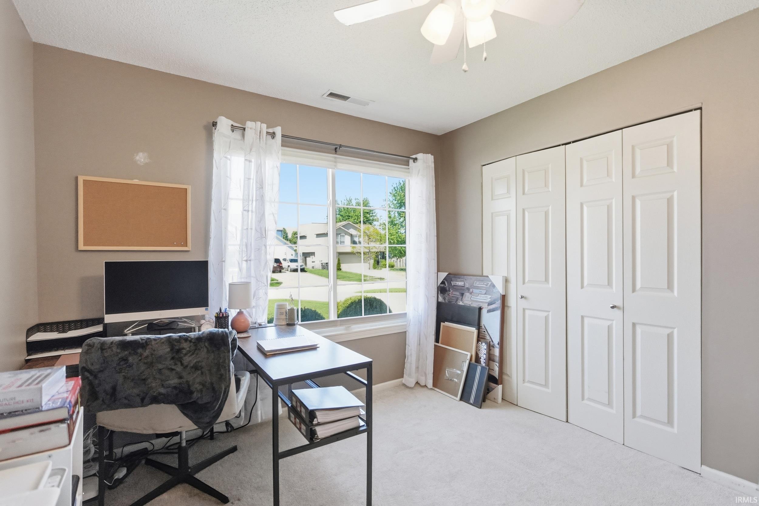 Carpeted room featuring a large window, a ceiling fan with integrated lighting, and bi-fold closet doors