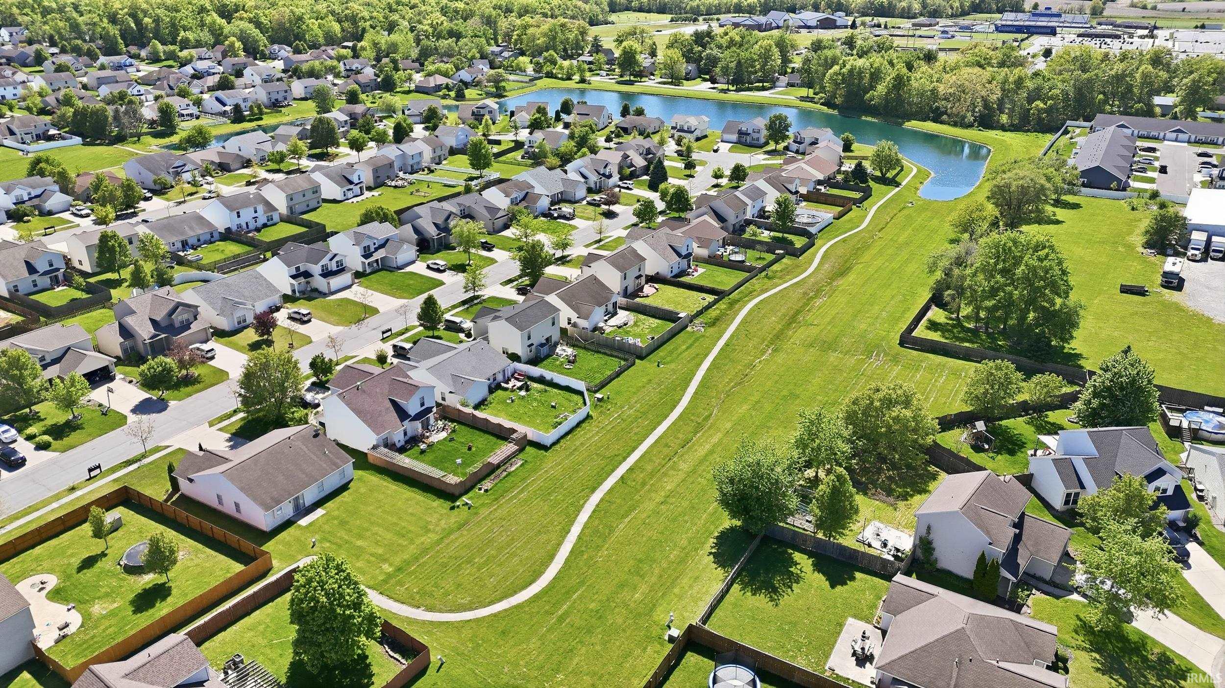 Aerial perspective of a developed residential area featuring single-family homes, manicured lawns, paved streets, and mature trees