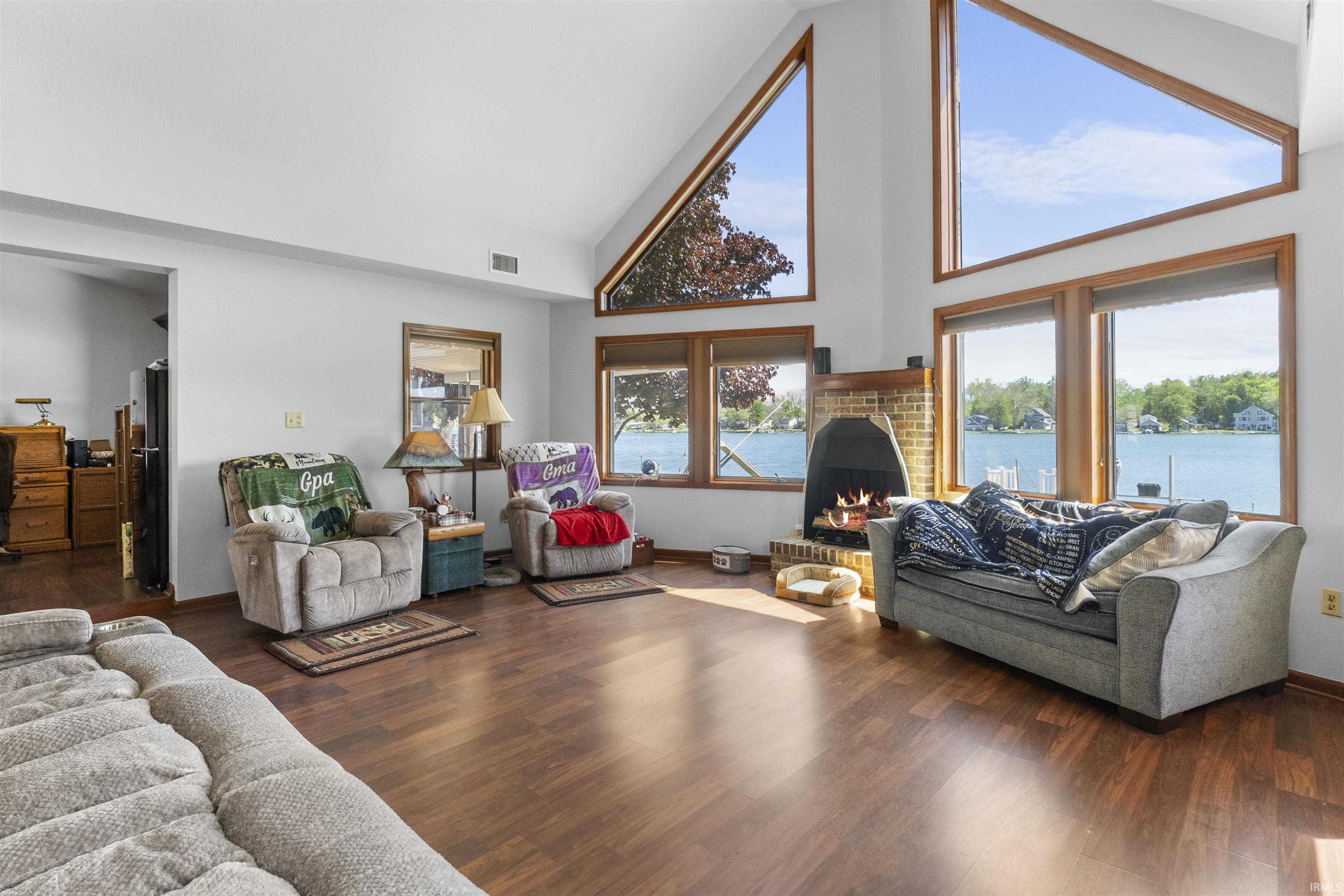 Spacious living area featuring expansive windows with water scenery, vaulted ceilings, and wood-finish flooring