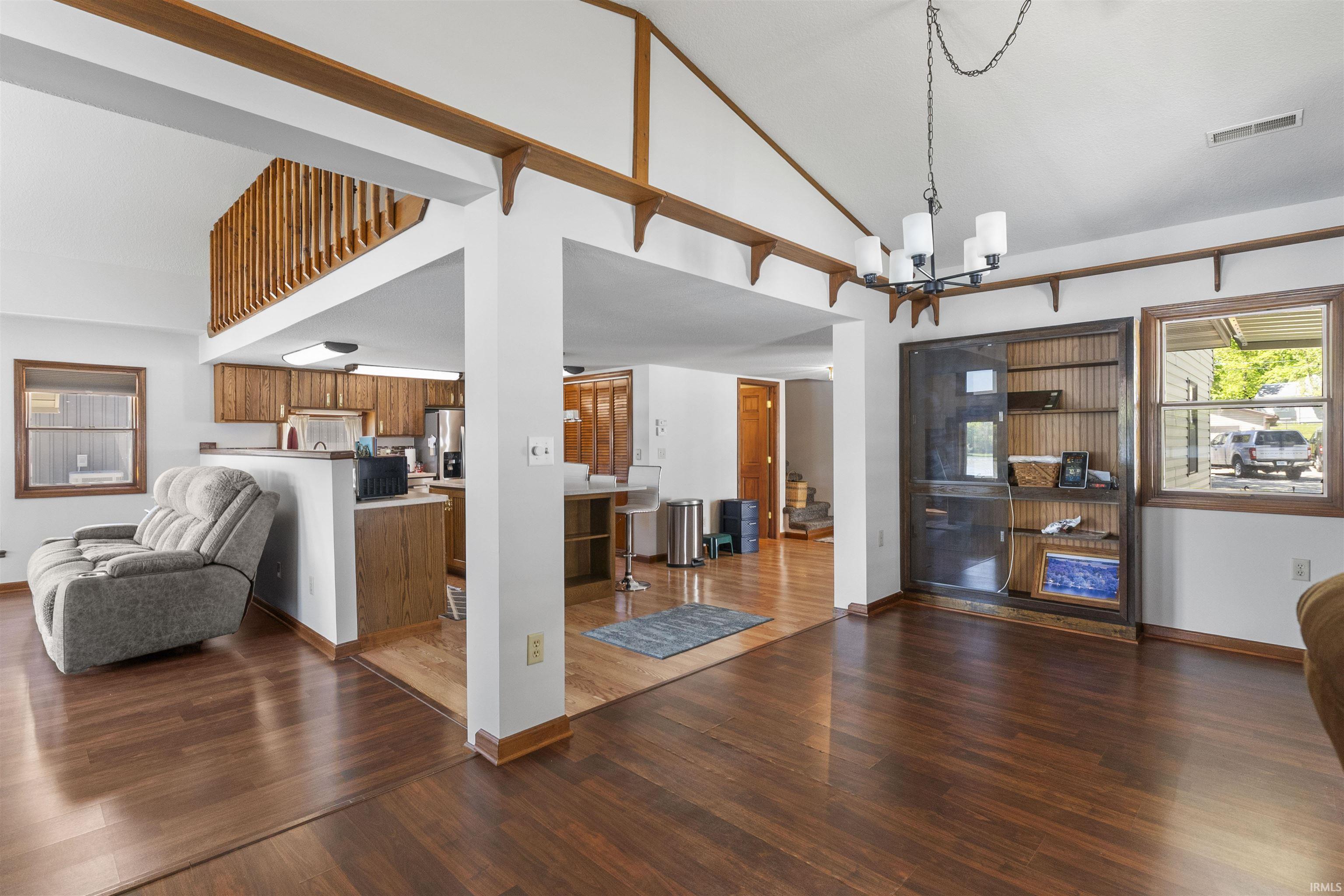 Open-concept living area featuring wood-finish flooring, a vaulted ceiling, and a built-in shelving unit