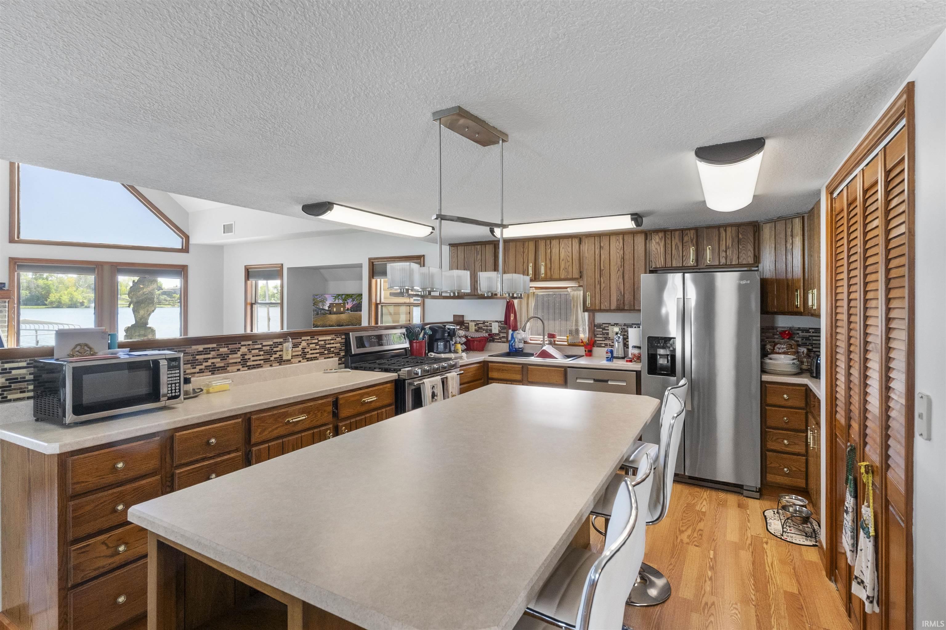 Kitchen featuring a large island, wood-finish flooring, stainless steel appliances, and wood cabinetry