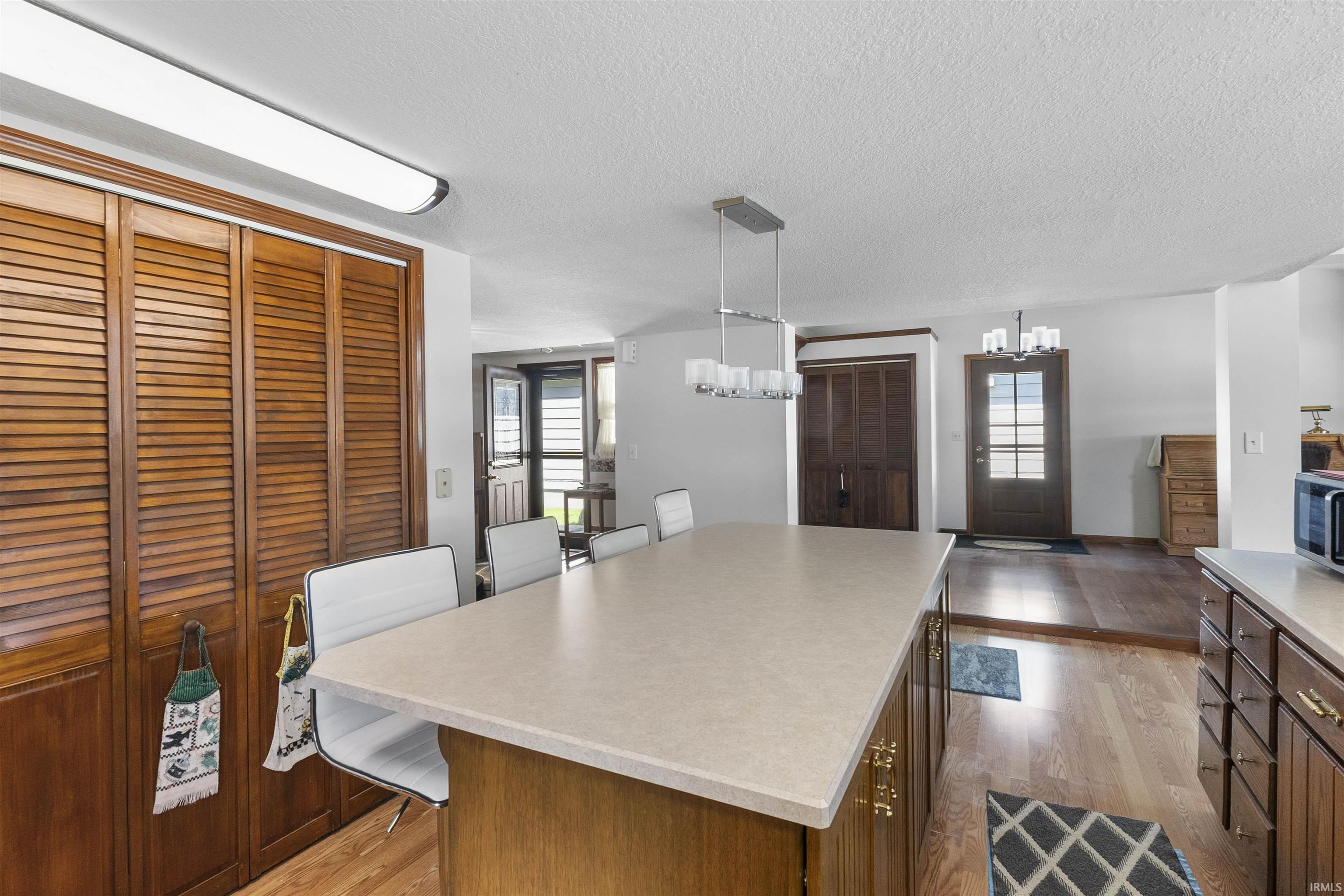 Kitchen featuring a large island with a light-toned countertop, wood-finish flooring, and a contemporary chandelier