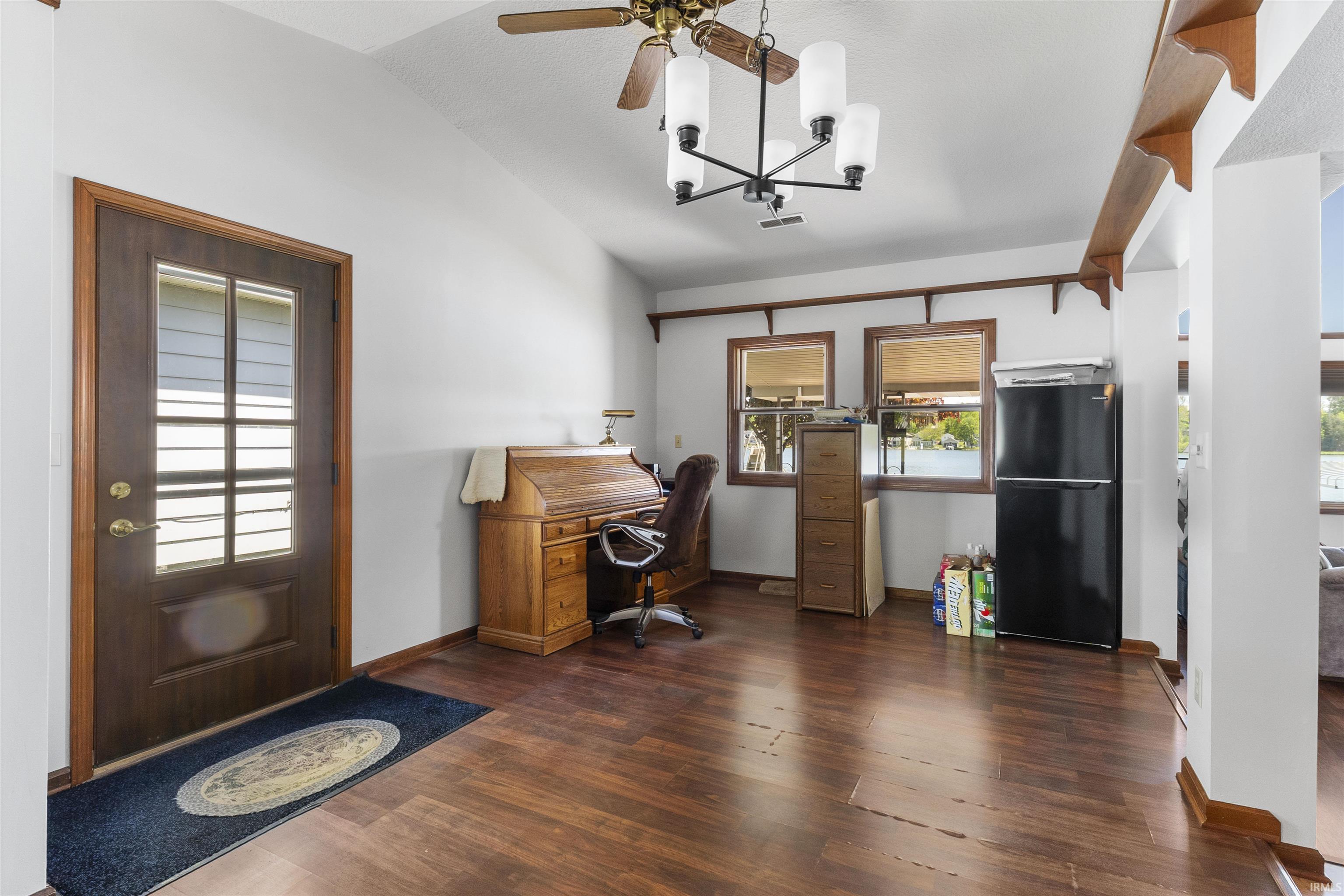 Open-concept room featuring wood-finish flooring, vaulted ceilings, and a ceiling fan with integrated lighting
