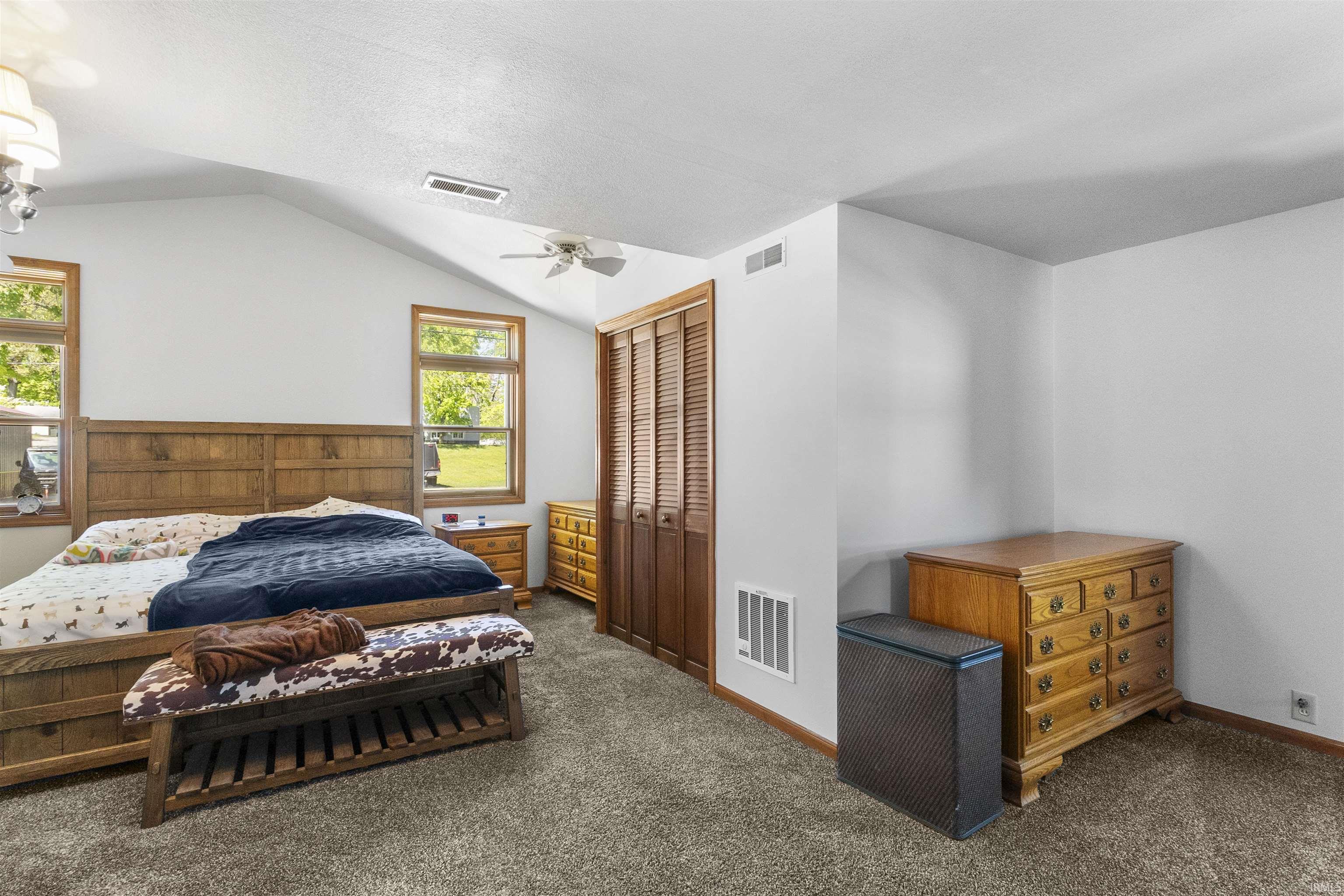 Bedroom featuring vaulted ceilings, two framed windows, wood-finish bi-fold closet doors, a ceiling fan, and carpet flooring