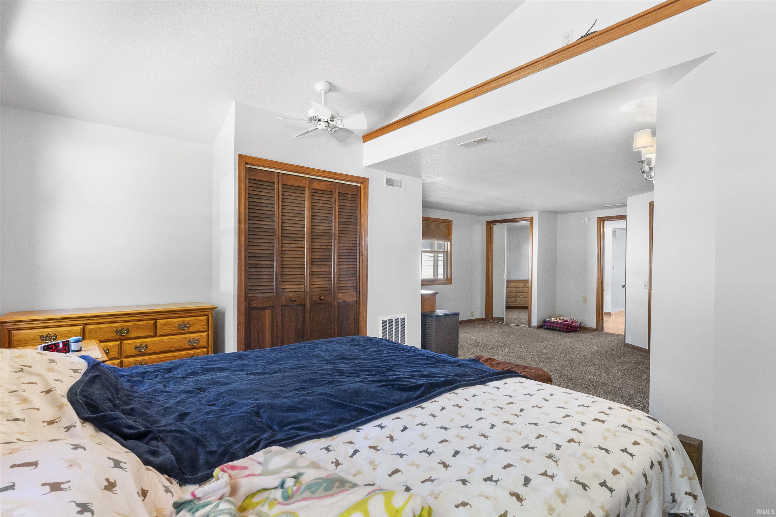 Vaulted ceiling featuring a ceiling fan, wood-finish louvered closet doors, and wood-finish trim accents