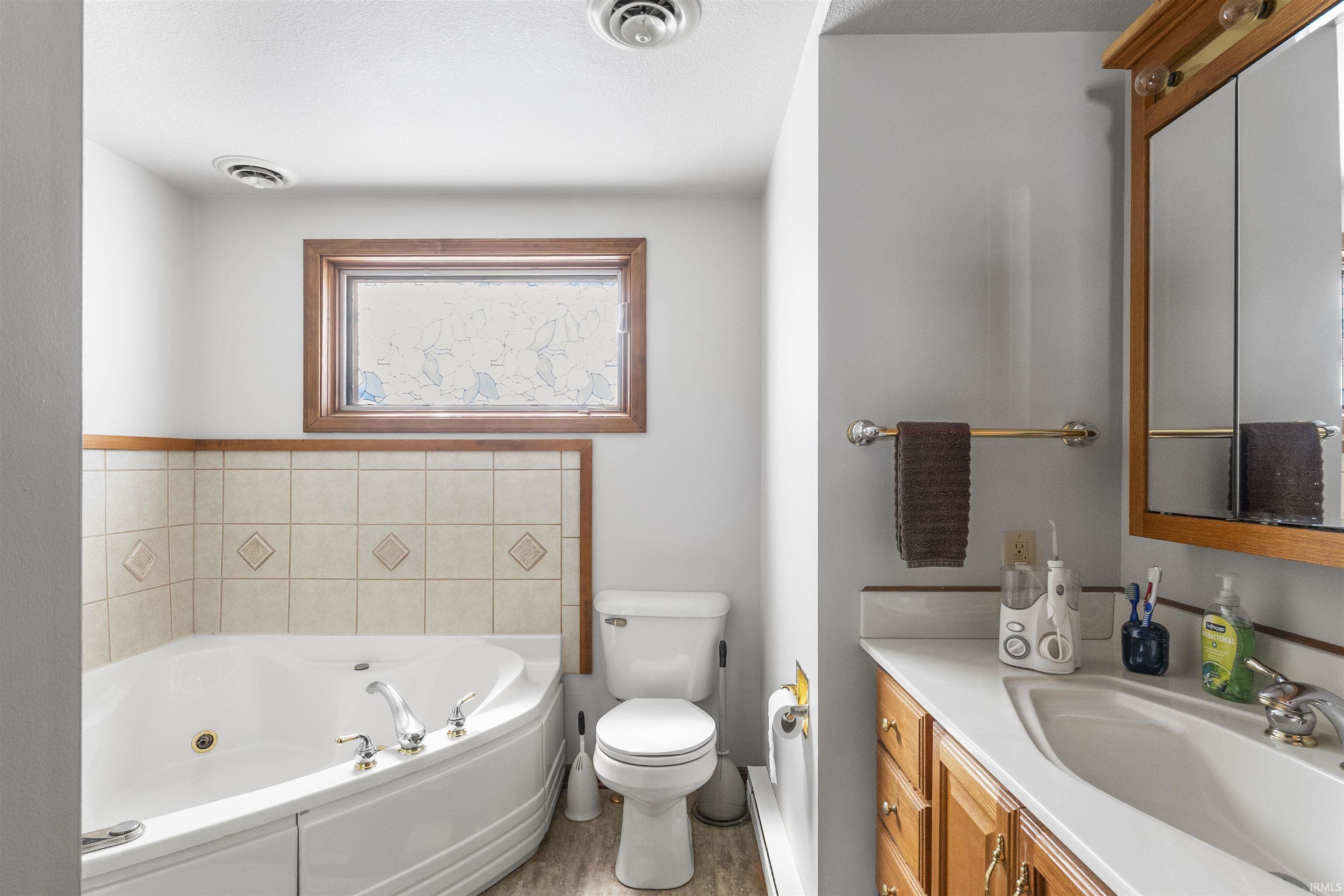 Bathroom featuring a corner soaking tub with tile surround, wood-frame window, and a vanity with a built-in sink and wood cabinetry