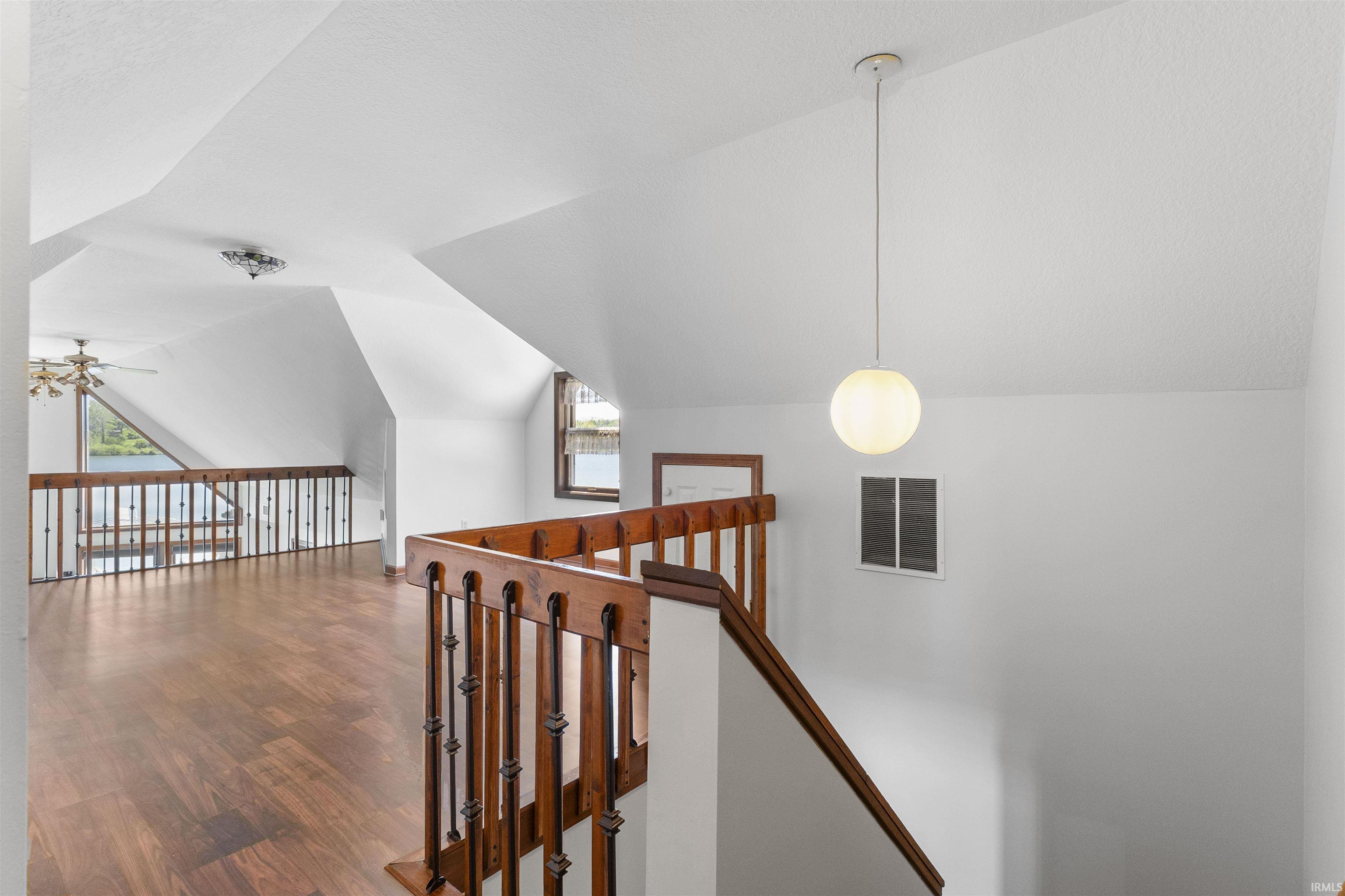 Upper-level landing featuring wood-finish flooring, a traditional wood banister, white walls, and a contemporary spherical pendant light