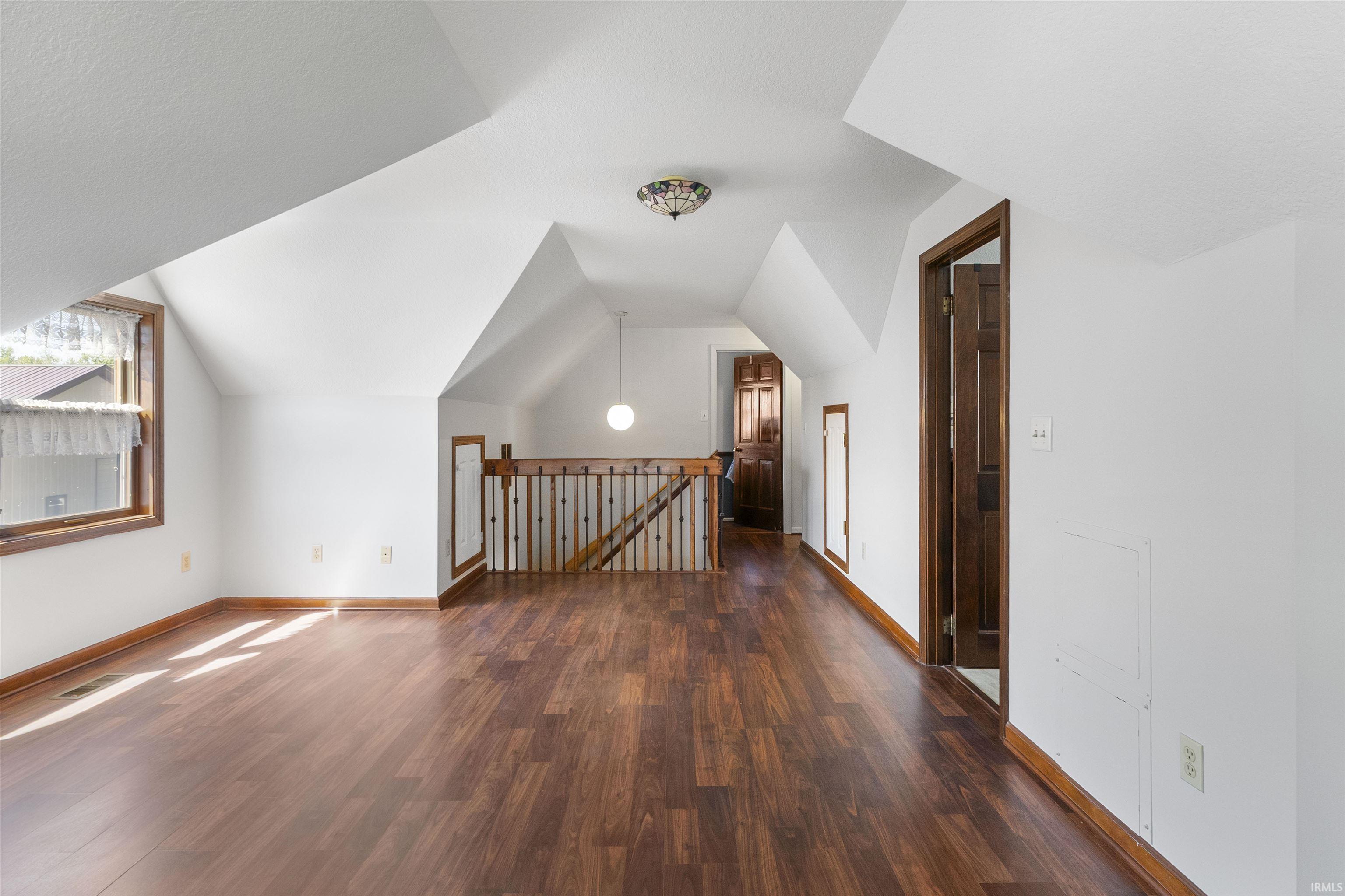 Spacious upper-level area featuring wood-finish flooring, white vaulted ceilings, and a light wood railing