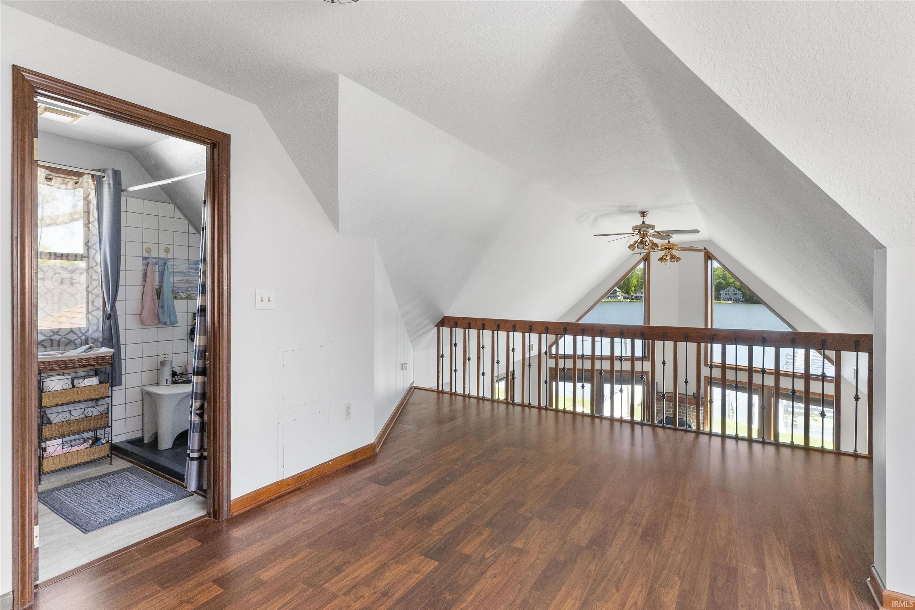 Spacious loft area featuring rich wood-finish flooring and a wood railing with metal spindles
