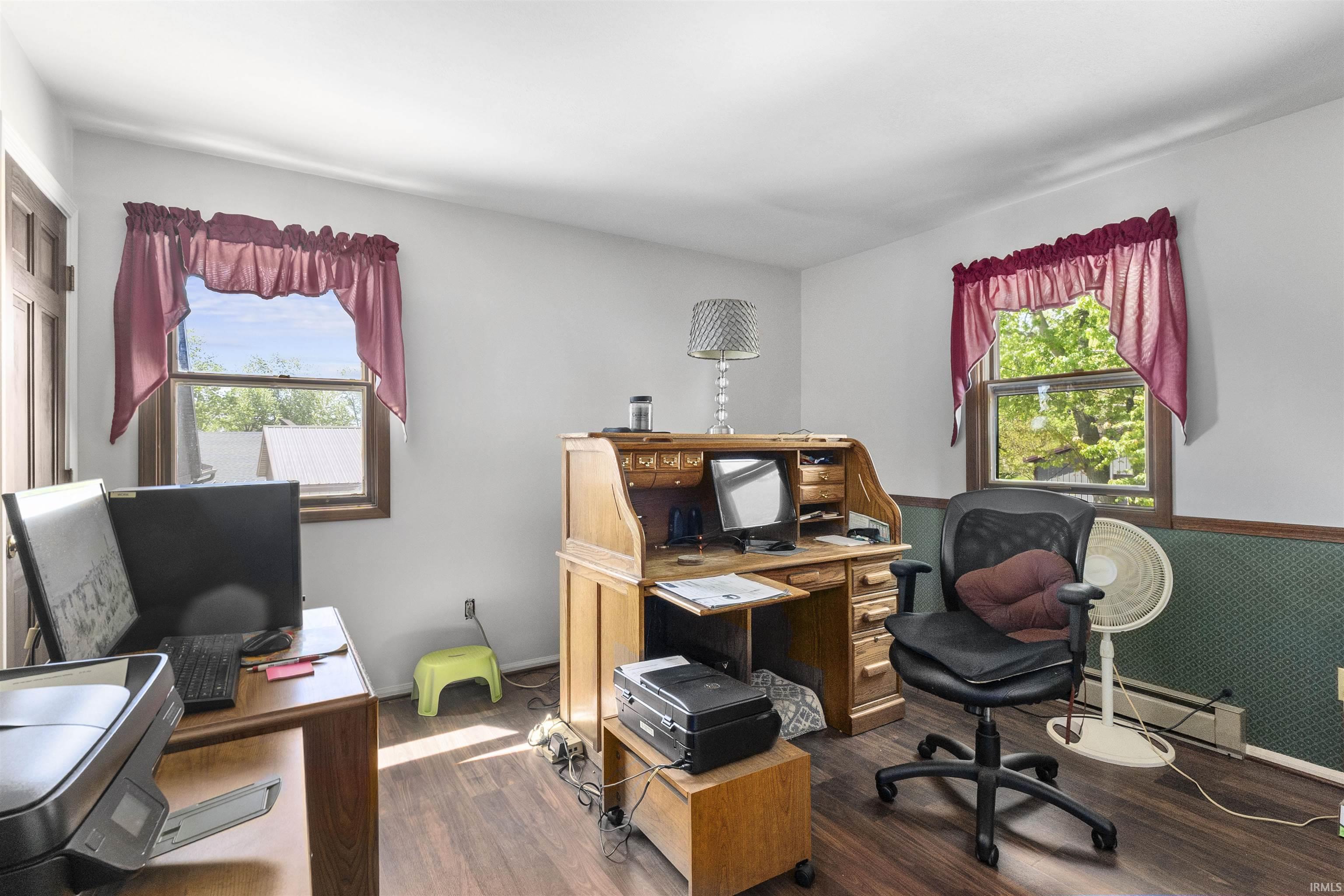 Room featuring wood-finish flooring, white walls, and two windows with wood trim