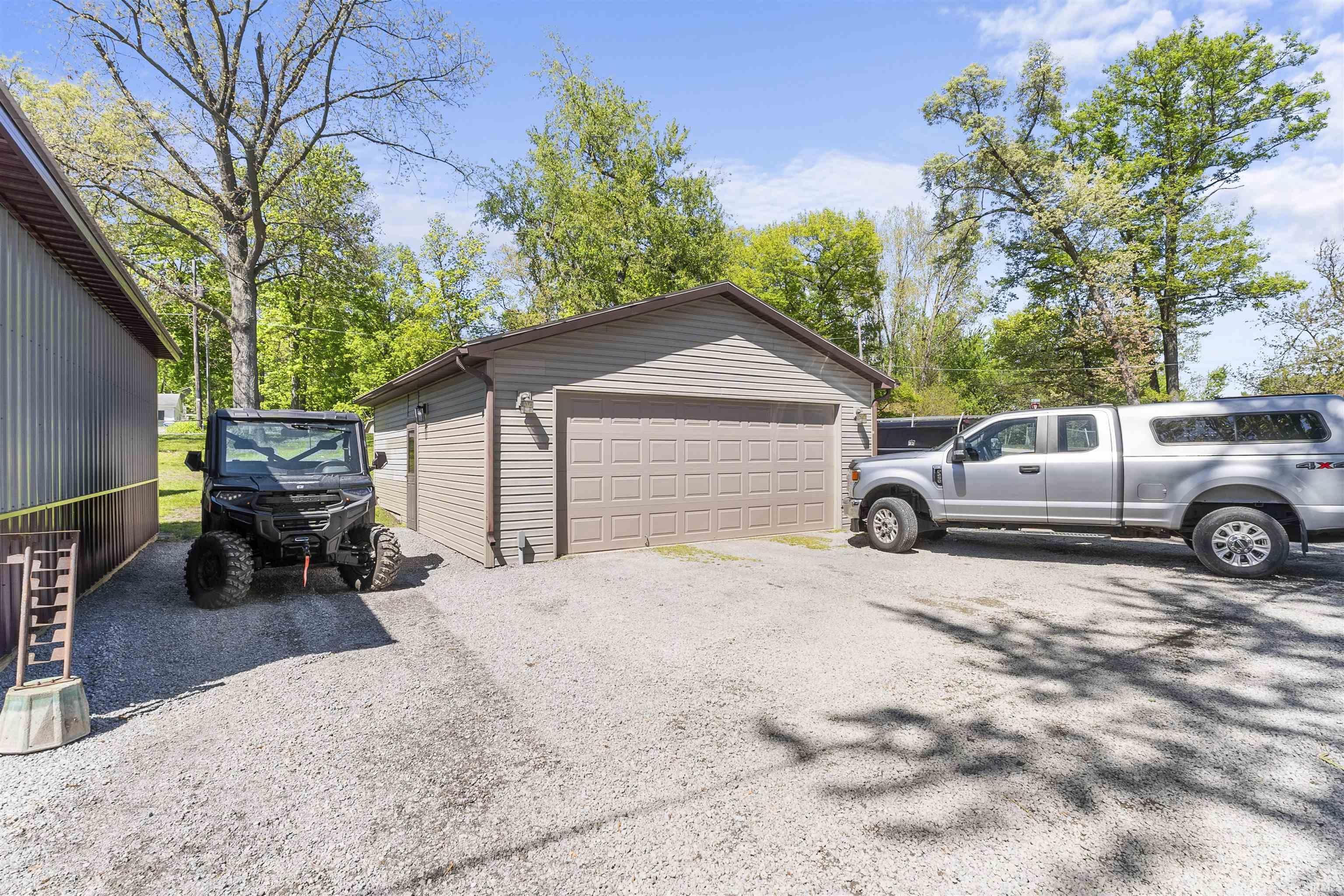 Gravel driveway offering ample parking, featuring a detached garage with a paneled overhead door and horizontal siding