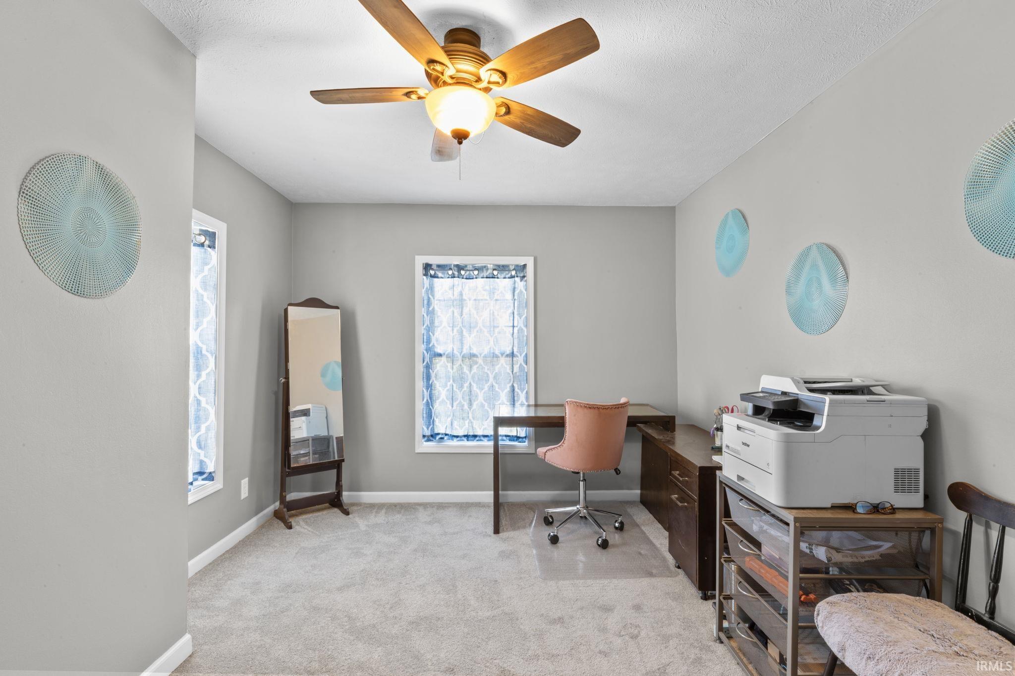 Carpeted room featuring a ceiling fan with integrated lighting, two windows with white trim, and light gray wall paint