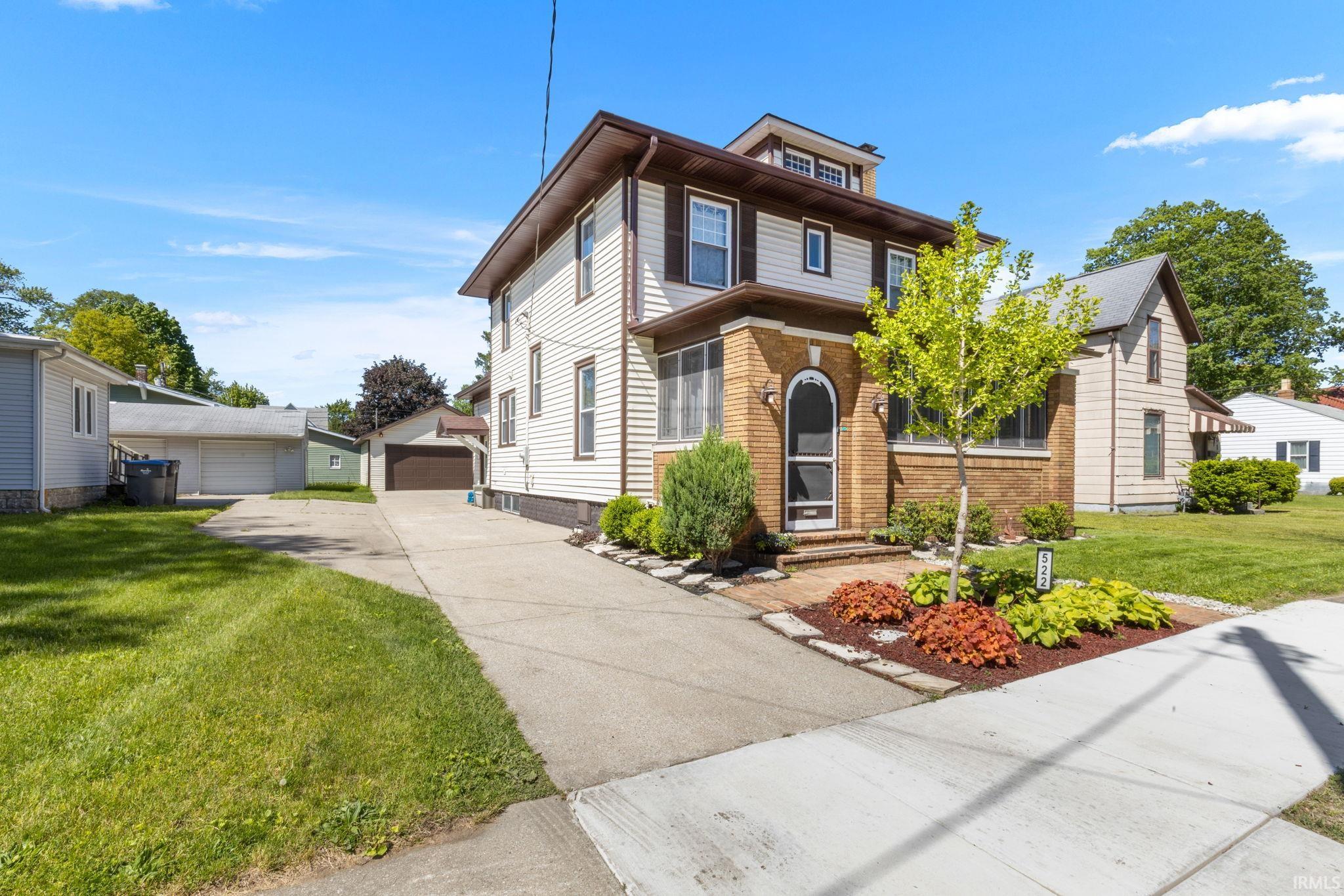 Two-story property featuring a brick and siding exterior, established front landscaping, an extended concrete driveway, and a detached garage