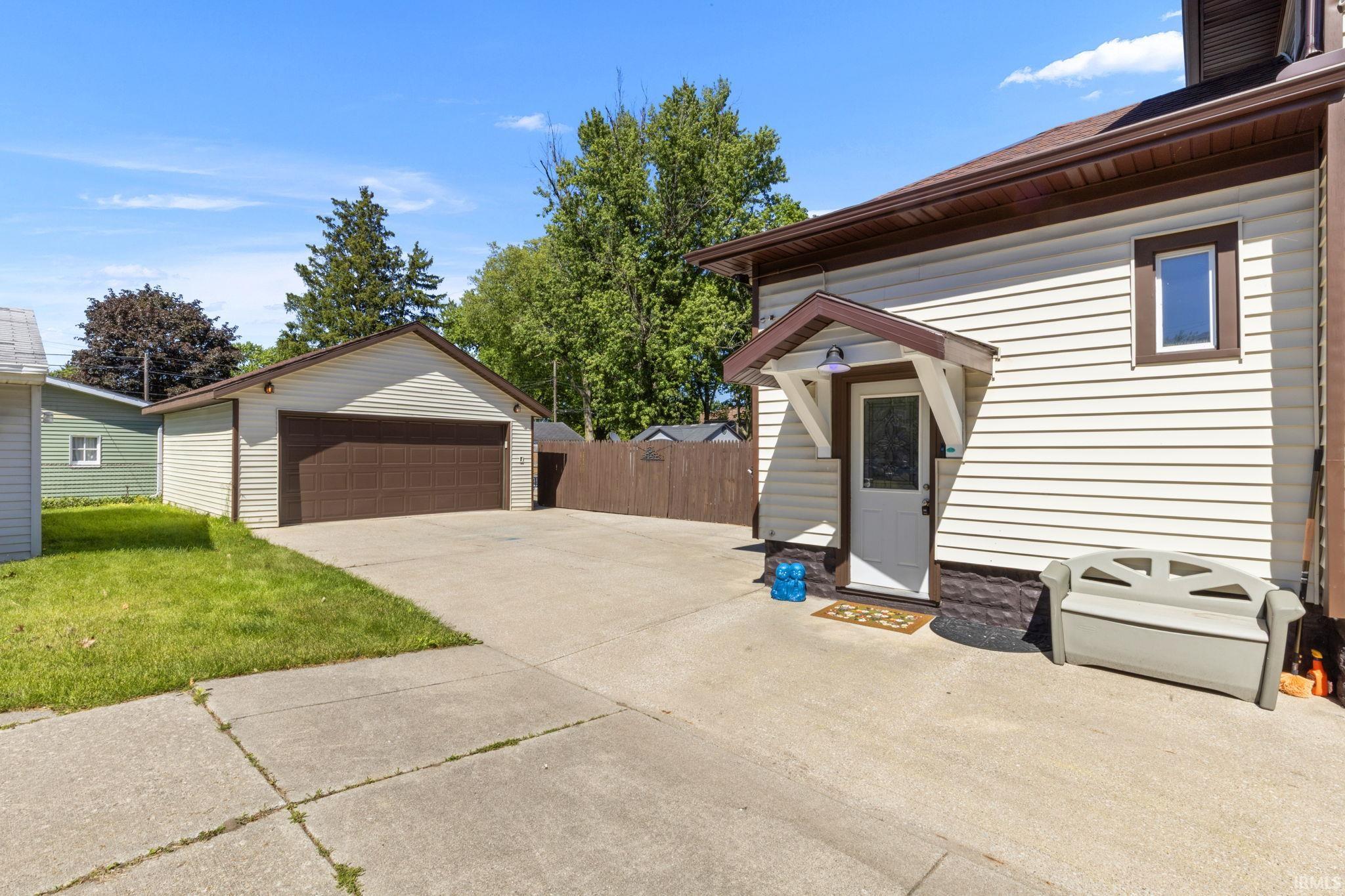Detached garage with a brown automatic door, concrete driveway, and side entry door with an overhang