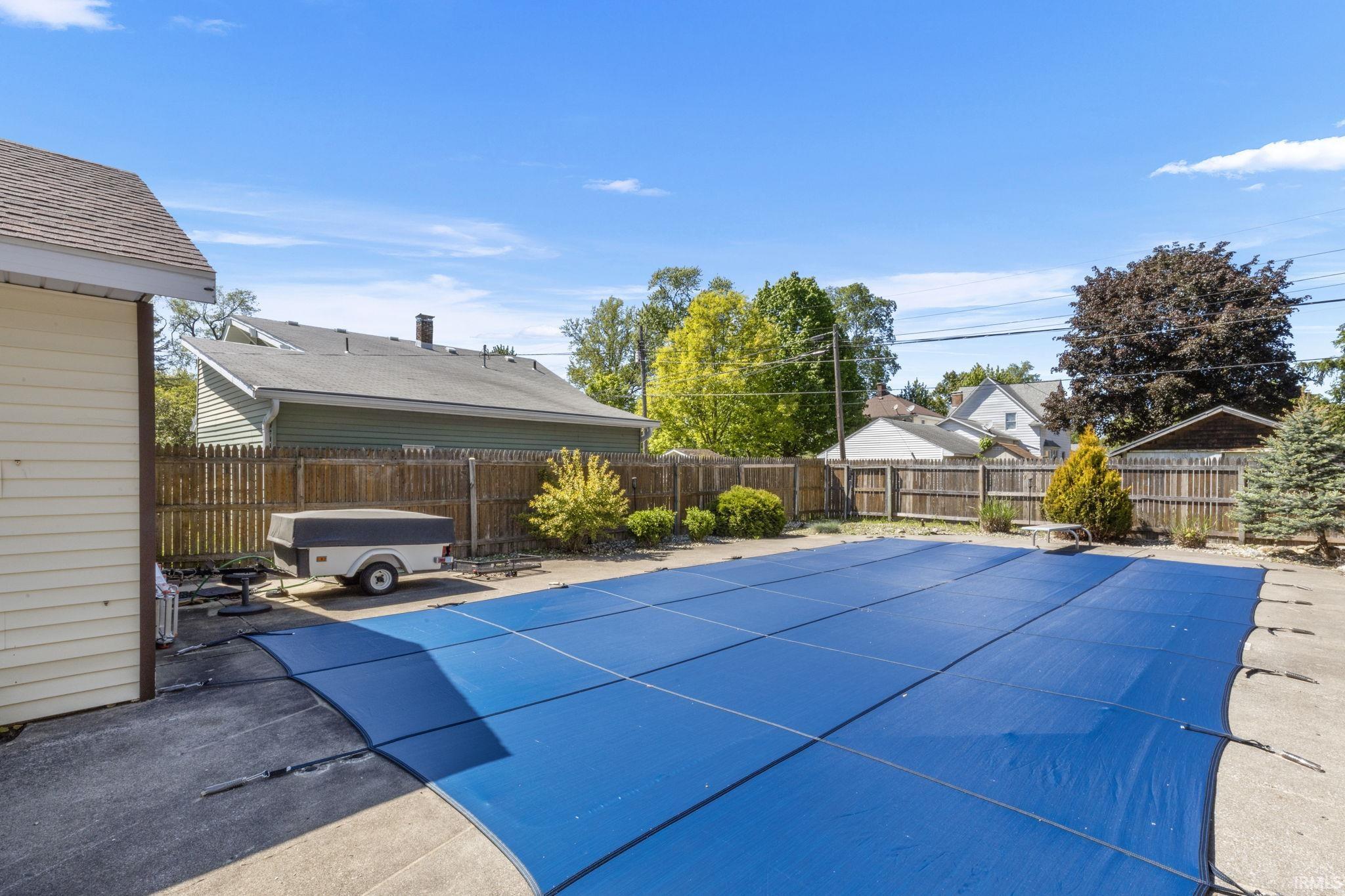 Outdoor swimming pool with a blue safety cover, surrounded by a concrete patio