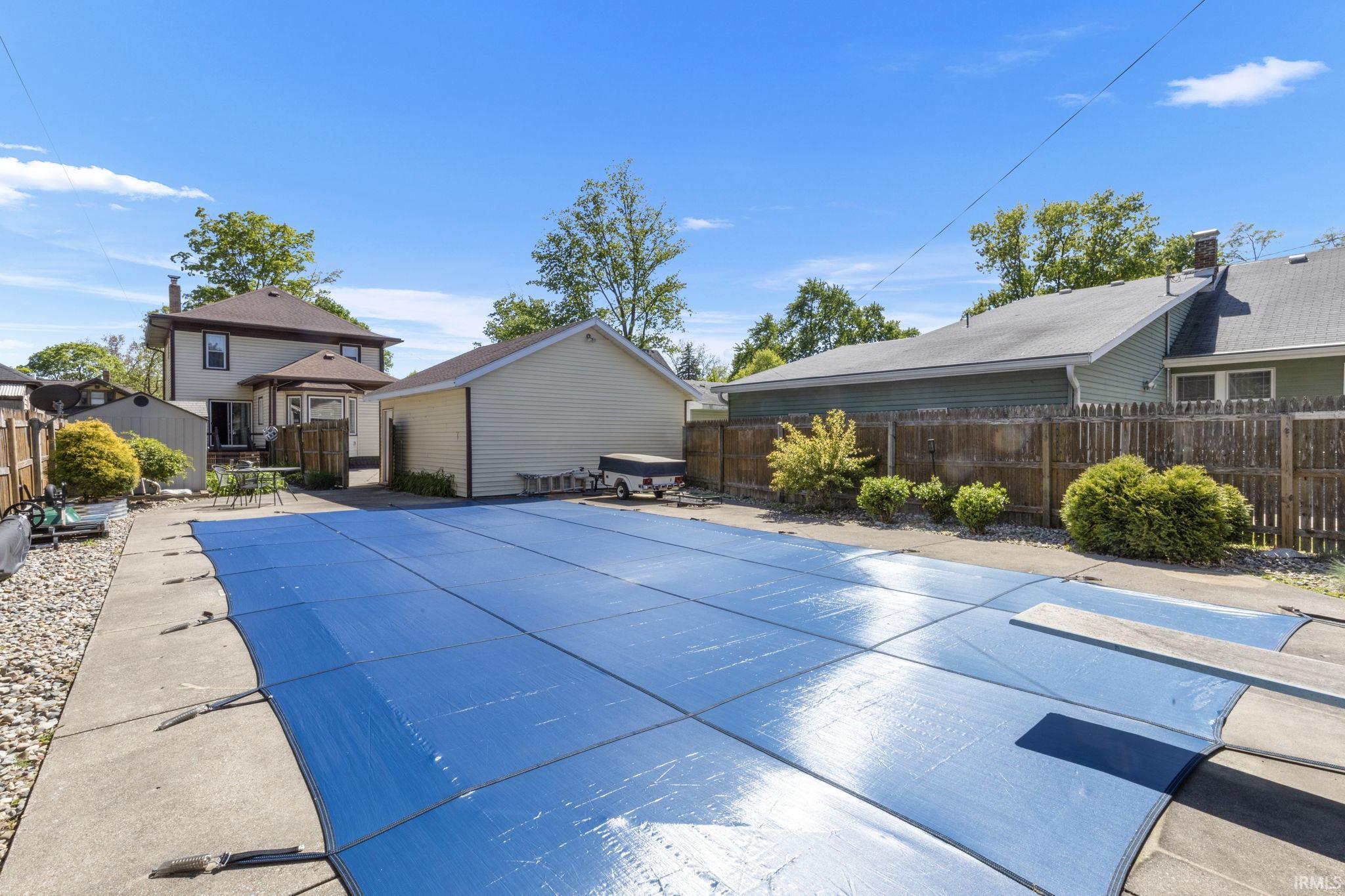 Expansive backyard featuring a covered pool, concrete patio, and mature landscaping