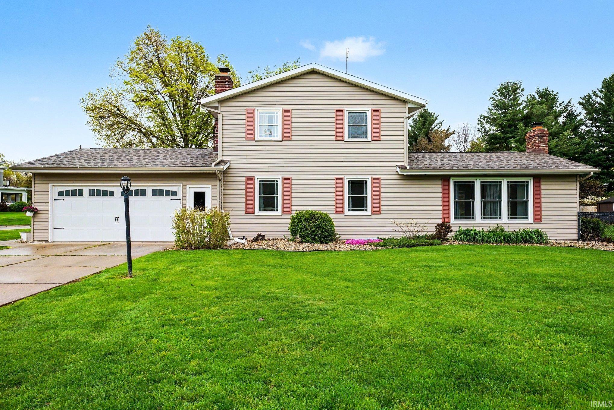 Two-story residence featuring light-toned siding, a two-car garage with white paneled doors, and red decorative window shutters