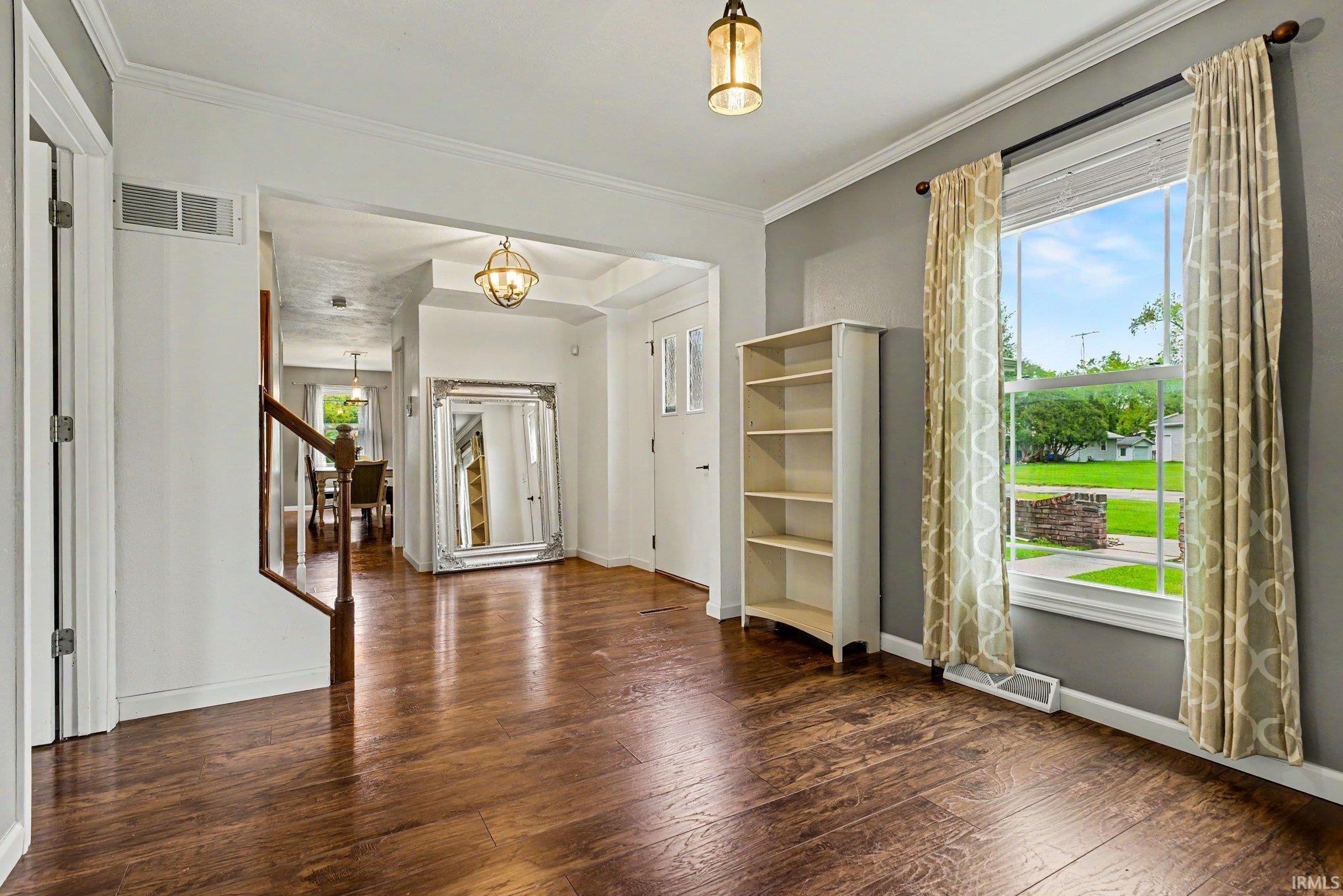 Rich wood-finish flooring extends throughout this open living space, featuring neutral wall tones, white trim, and a window offering abundant natural light