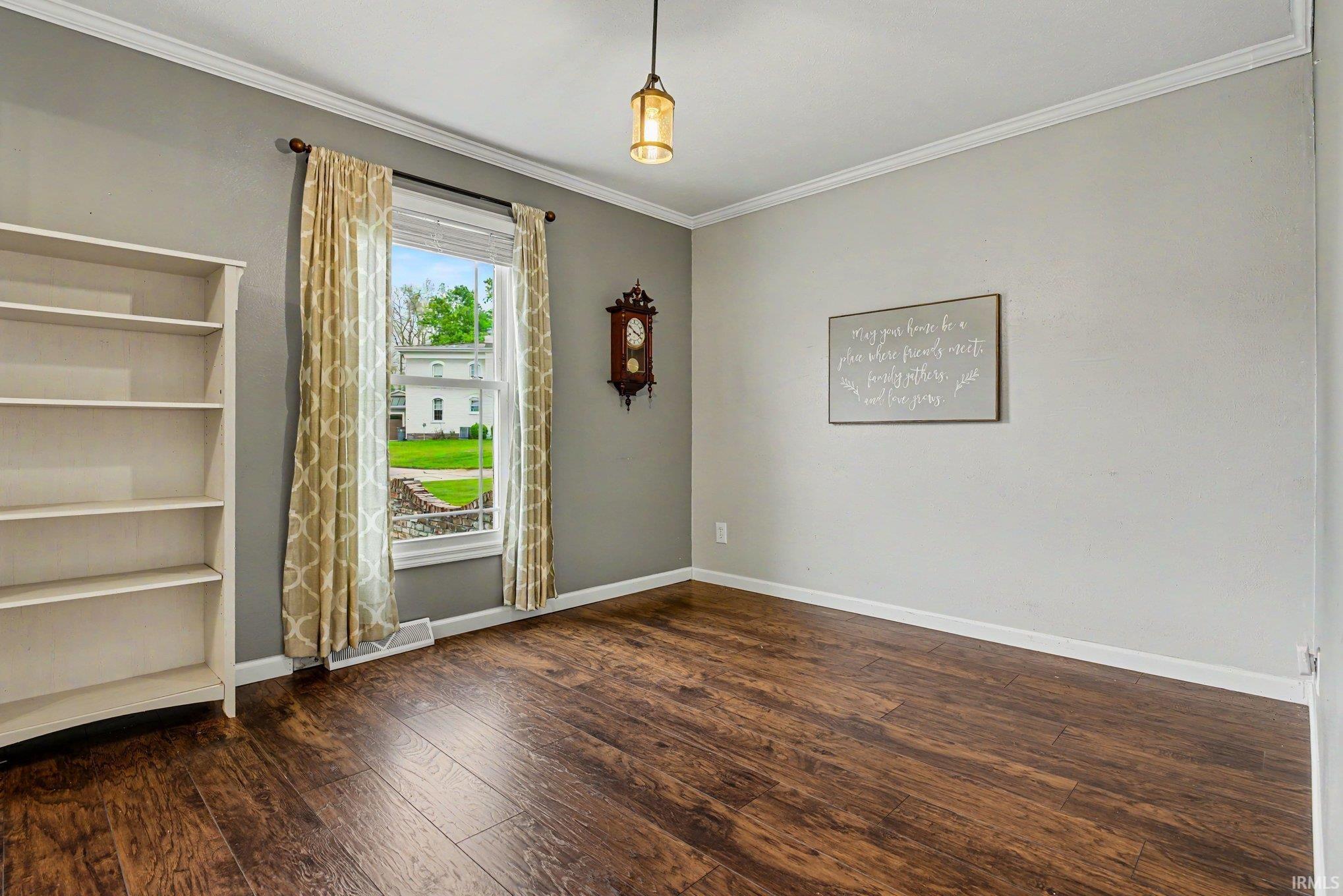 Spacious room with dark wood-finish flooring, light grey walls, and white crown molding
