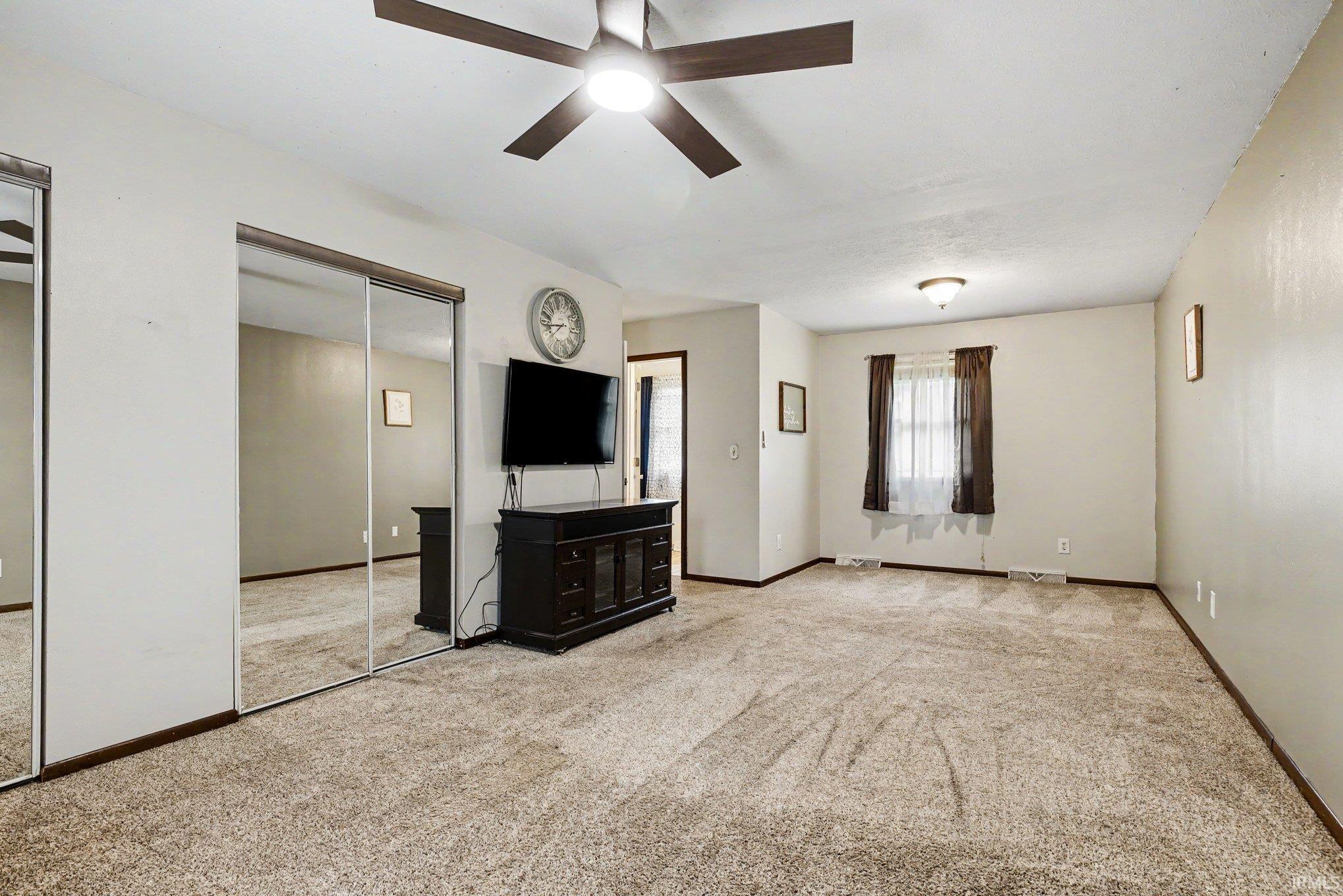 Spacious room featuring neutral carpet flooring, light-toned wall paint, and a ceiling fan